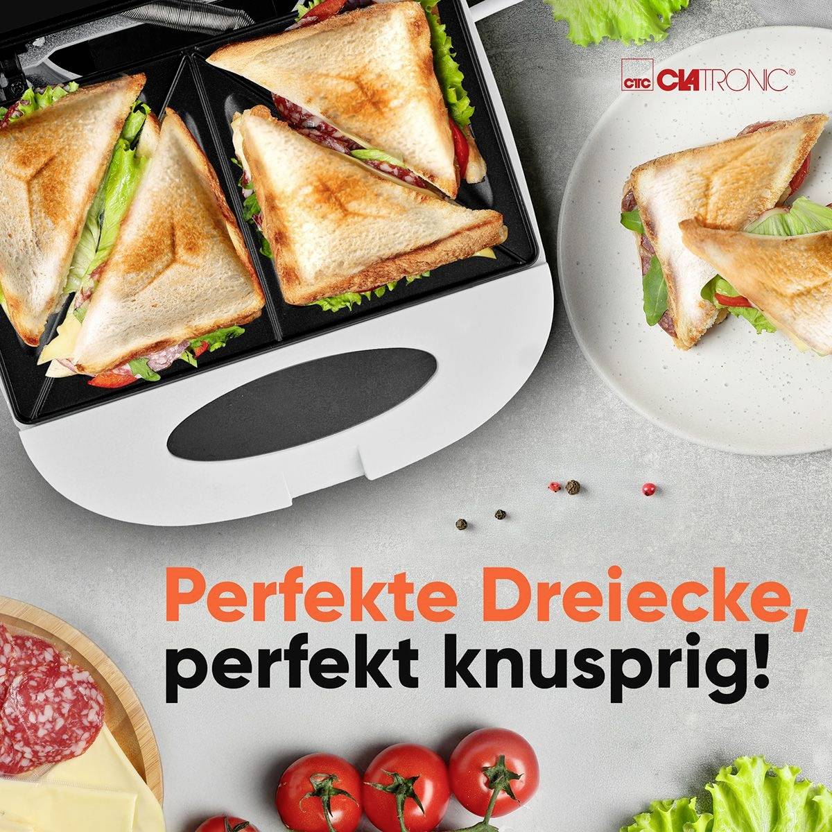 Sandwichmaker mit gegrillten Sandwiches, gefüllt mit Salat und Schinken. Unten liegen frische Zutaten wie Salat, Tomaten und Käse.