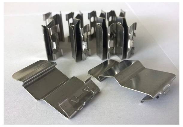 Metalclips in unterschiedlichen Formen und Größen, auf einer weißen Fläche liegend, zeigen ihre reflektierende Metalloberfläche.