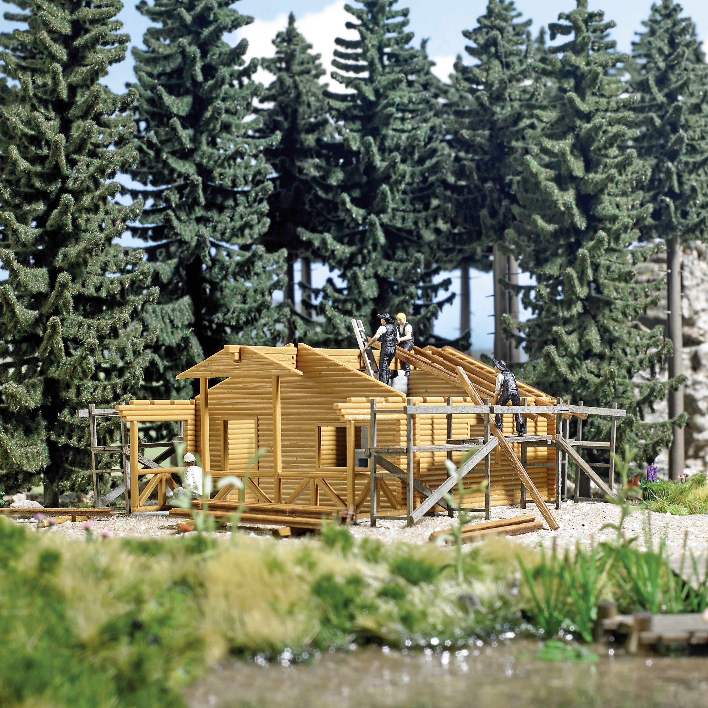 Modell eines Holzhauses im Bau, umgeben von Kiefernwald. Drei Figuren arbeiteten mit Holzbohlen und Balken beim Bau.