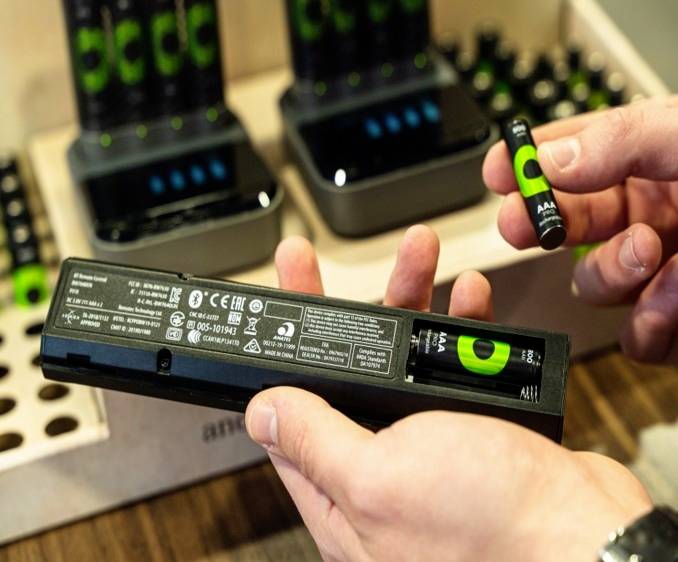 Eine Person hält eine Fernbedienung, die mit wiederaufladbaren AA-Batterien betrieben wird, vor einem Ladegerät.