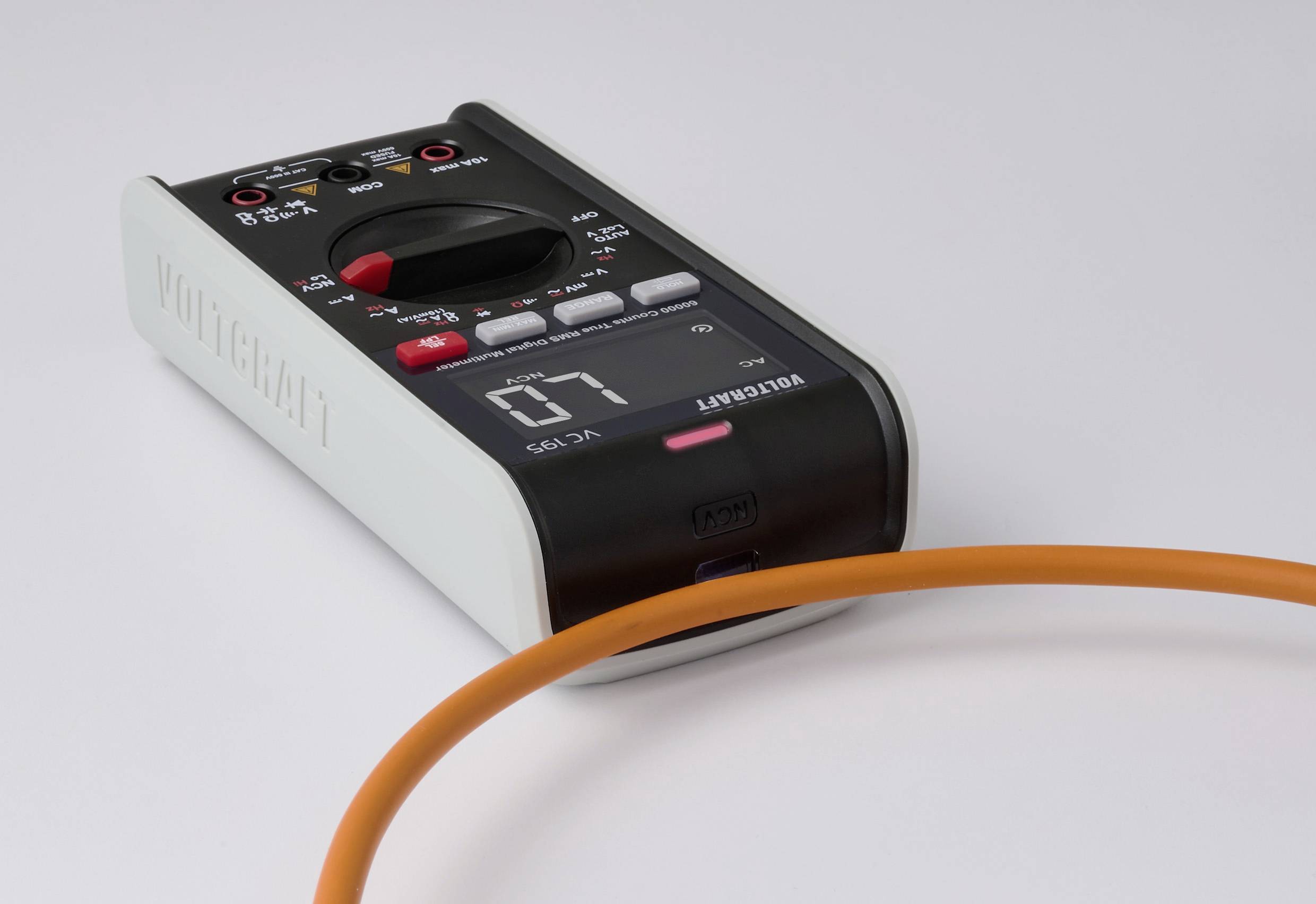 Ein digitales Multimeter mit schwarzem Frontpanel, das '07' anzeigt, liegt auf einer Oberfläche. Eine orangefarbene Kabelschleife ist im Vordergrund teilweise zu sehen.