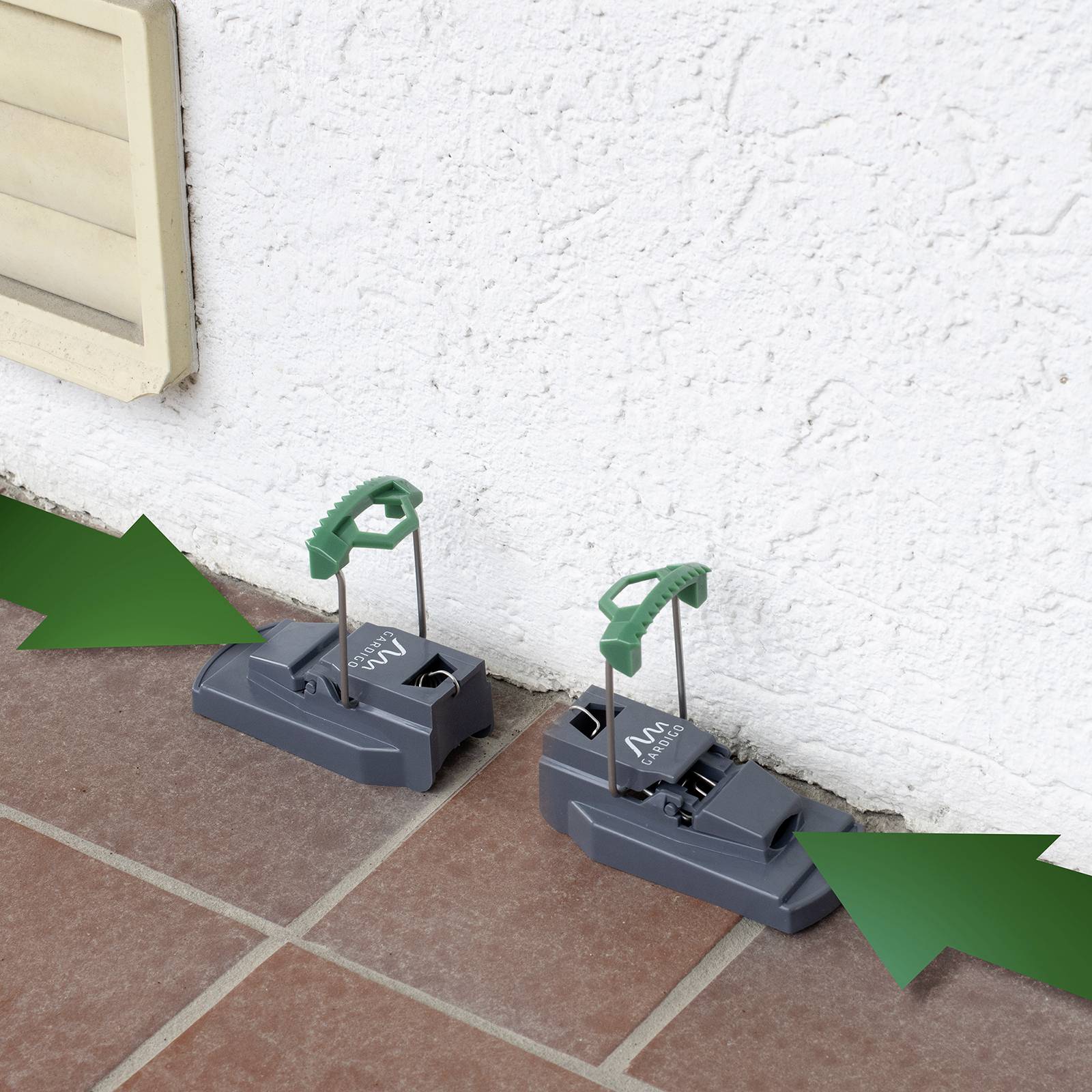 Zwei graue Fallen mit grünen Griffen an einer weißen Wand auf Terrassenfliesen, bereitgestellt zur Schädlingsbekämpfung.