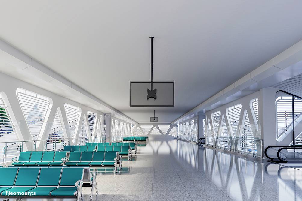 Lichter Wartebereich in einem modernen Flughafen mit grünen Sitzbänken und großen Fenstern. Leere Rolltreppen im Hintergrund.