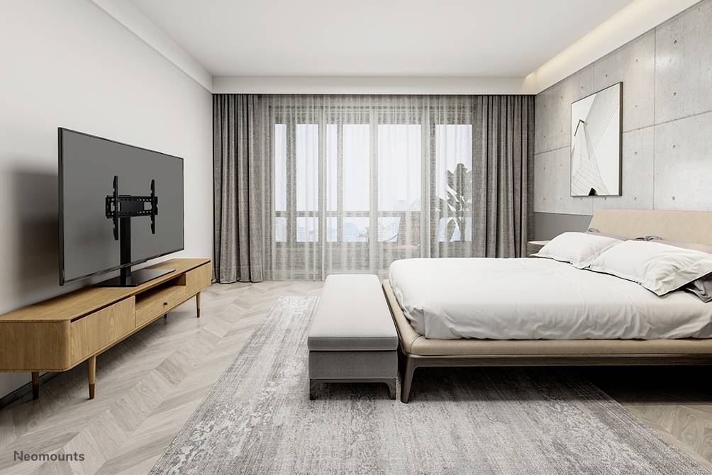 Ein modernes Schlafzimmer mit einem großen Bett, einem Holznachttisch und einem Flachbildfernseher an der Wand. Helle Fenster im Hintergrund.