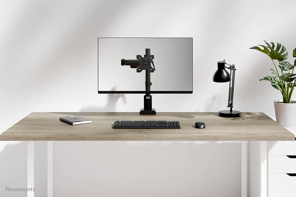 Ein moderner Schreibtisch mit Monitor, Tastatur, Maus, Lampe, einem Notizbuch und einer Pflanze. Minimalistisches Design.