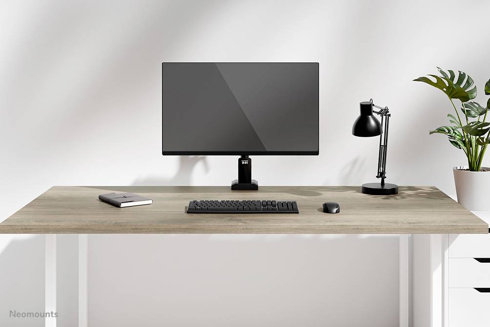 Ein minimalistischer Schreibtisch mit einem Monitor, Tastatur, Maus, Lampe, Notizbuch und einer Pflanze.