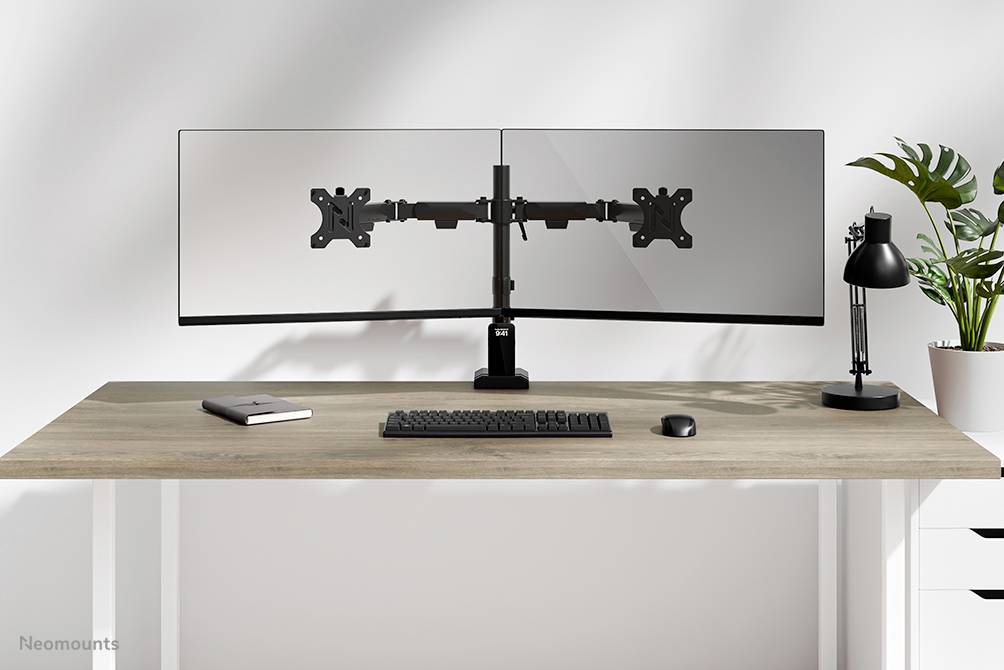 Zwei Monitore auf einem Schreibtisch mit Tastatur und Maus, links ein Notizbuch, rechts eine Lampe und Pflanzen im Hintergrund.