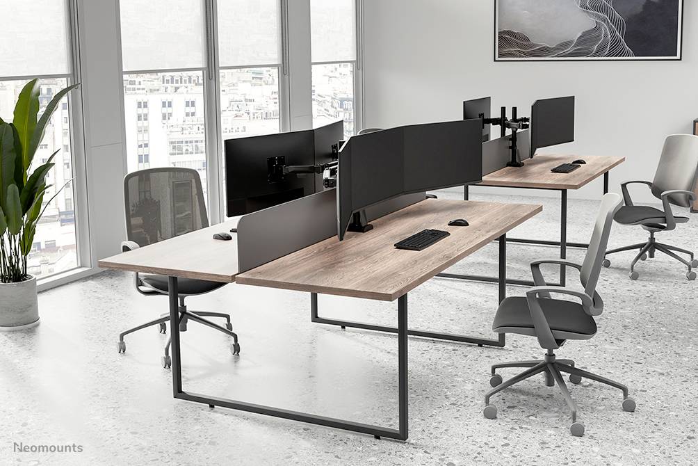 Moderne Büroräume mit mehreren Schreibtischen und Monitoren, ergonomische Stühle. Große Fenster mit Stadtblick im Hintergrund.