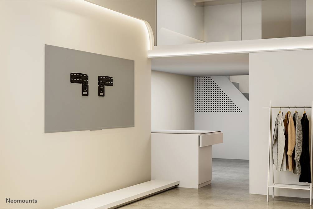 Wand mit TV-Halterung in modernem, minimalistischem Wohnraum. Rechts Kleiderständer mit Kleidungsstücken, im Hintergrund ein weißer Empfangstresen.