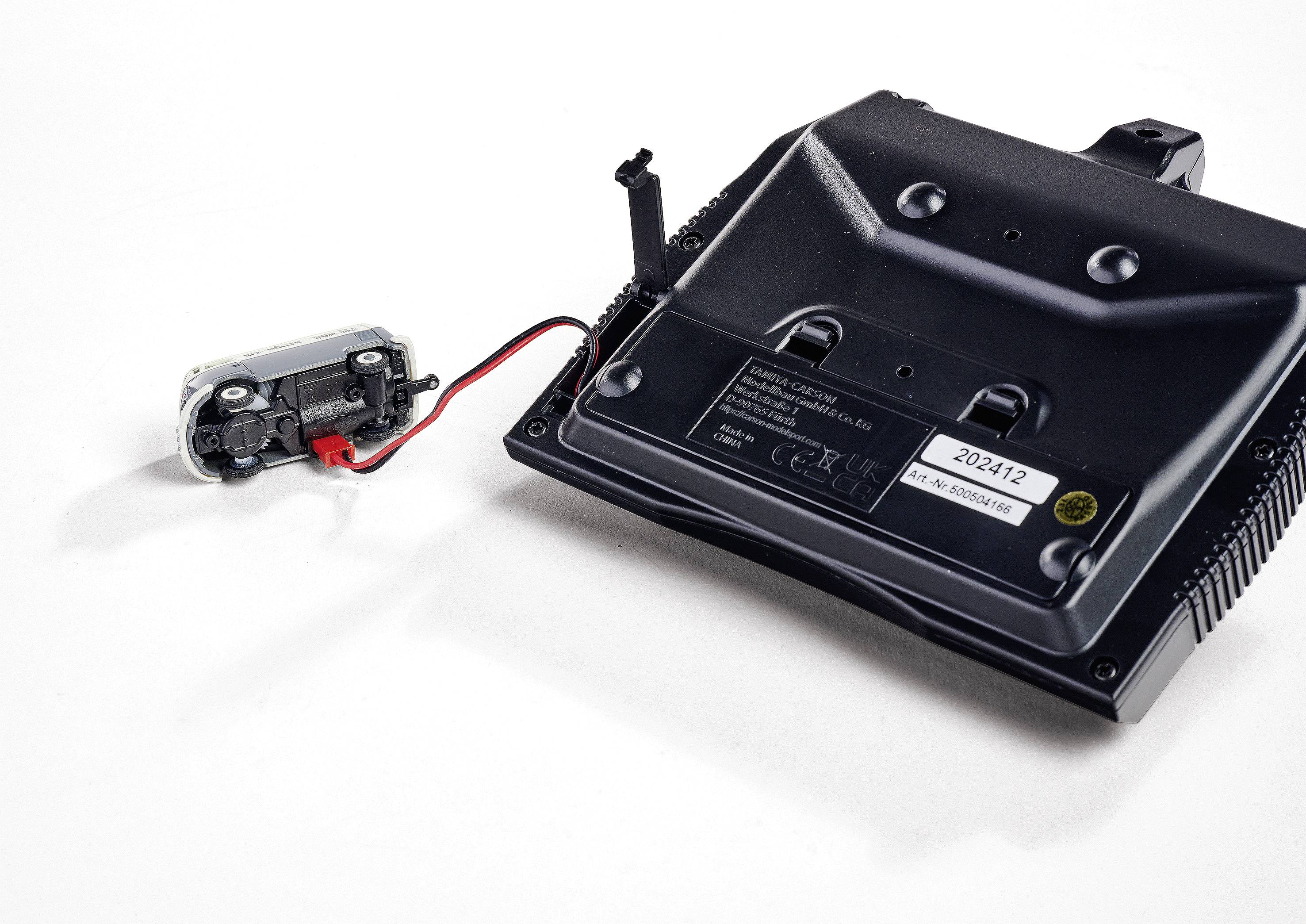 Schwarzes technisches Gerät mit verschiedenen Anschlüssen und einem angebrachten kleineren Modul mit rotem und schwarzem Kabel.
