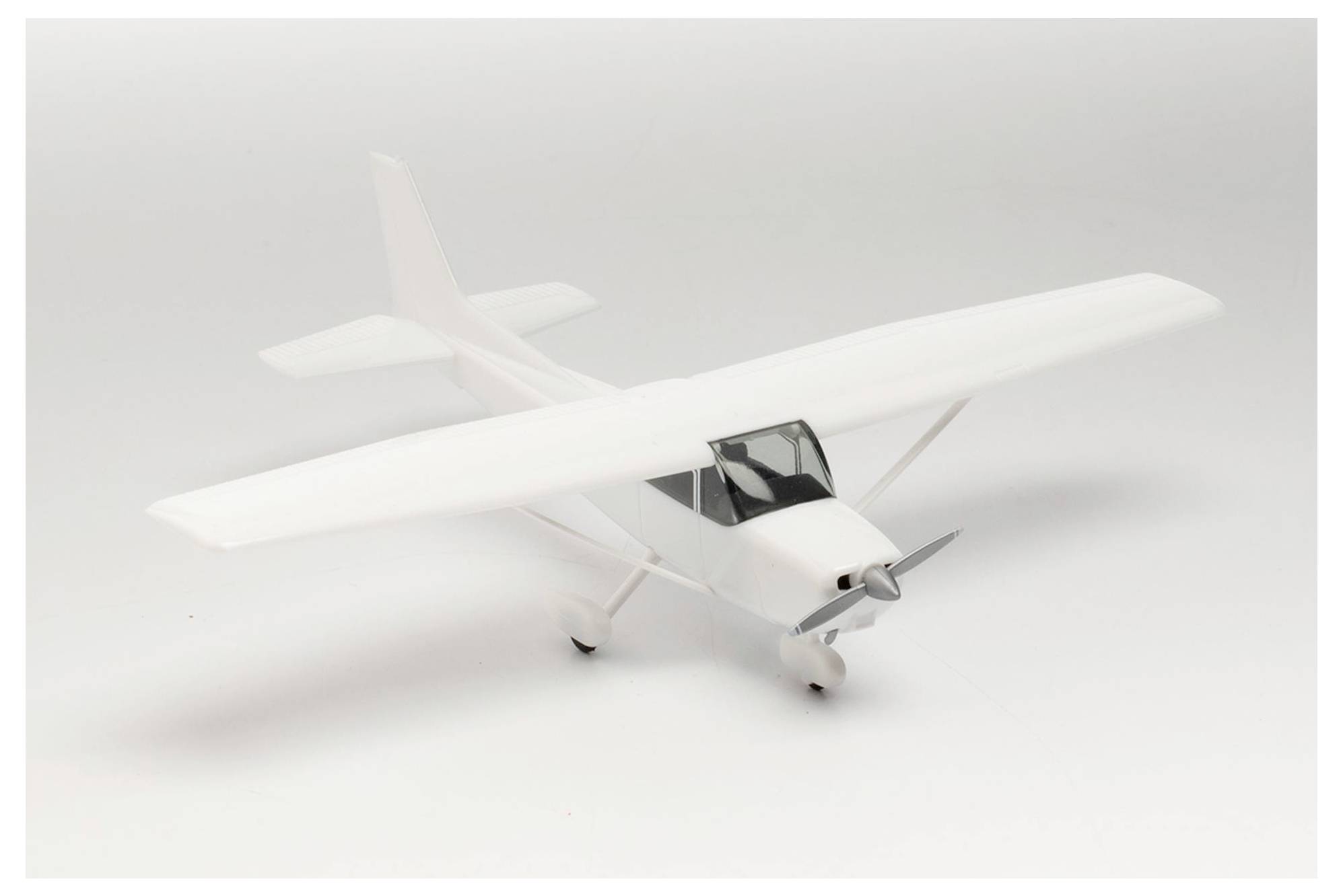 Ein weißes Modellflugzeug steht auf einem weißen Hintergrund. Es zeigt eine einmotorige Propellermaschine mit zwei Flügeln.