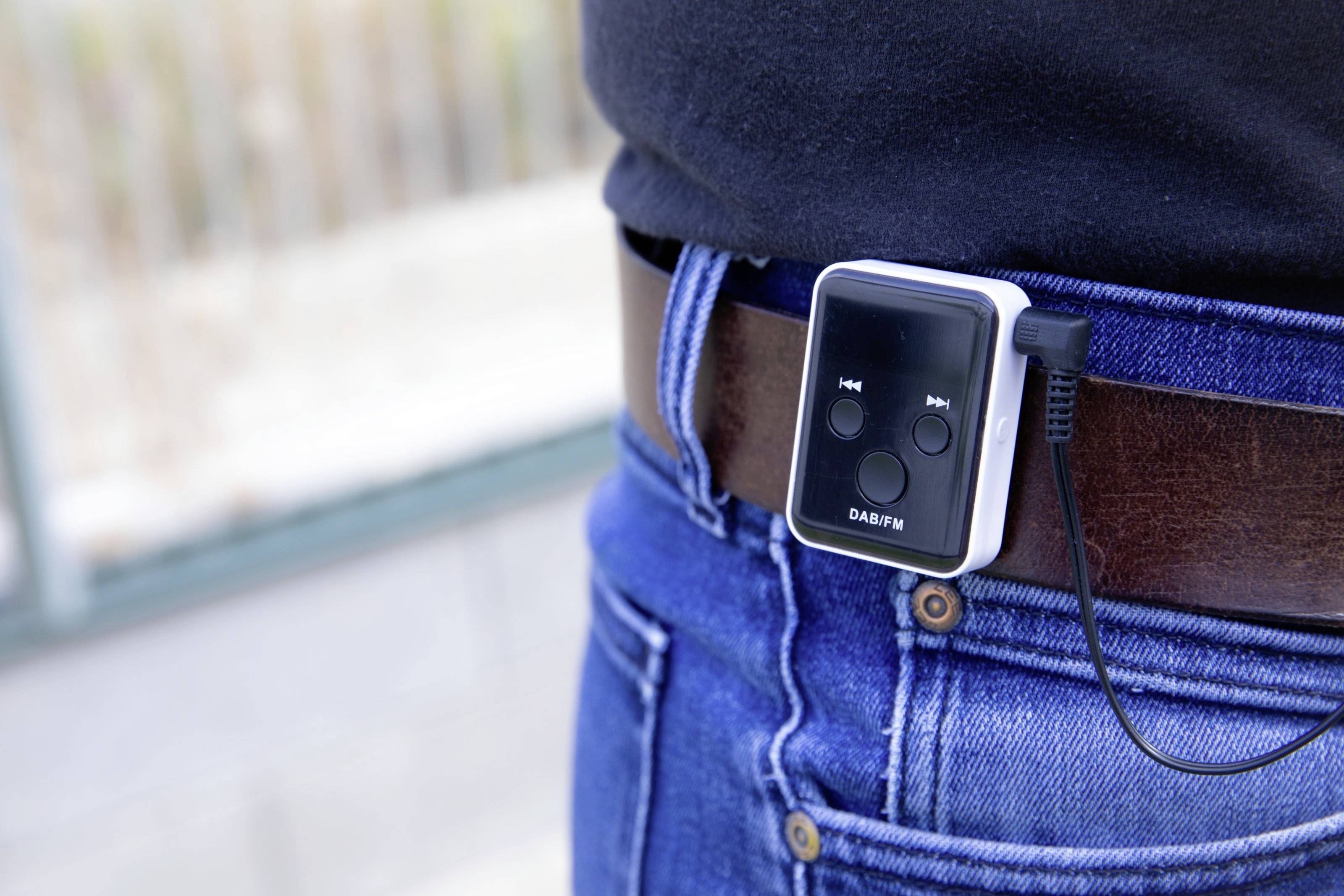 Ein tragbares DAB-Radio ist an einem braunen Gürtel an der Hüfte einer Person befestigt und zeigt Bedientasten auf der Vorderseite.