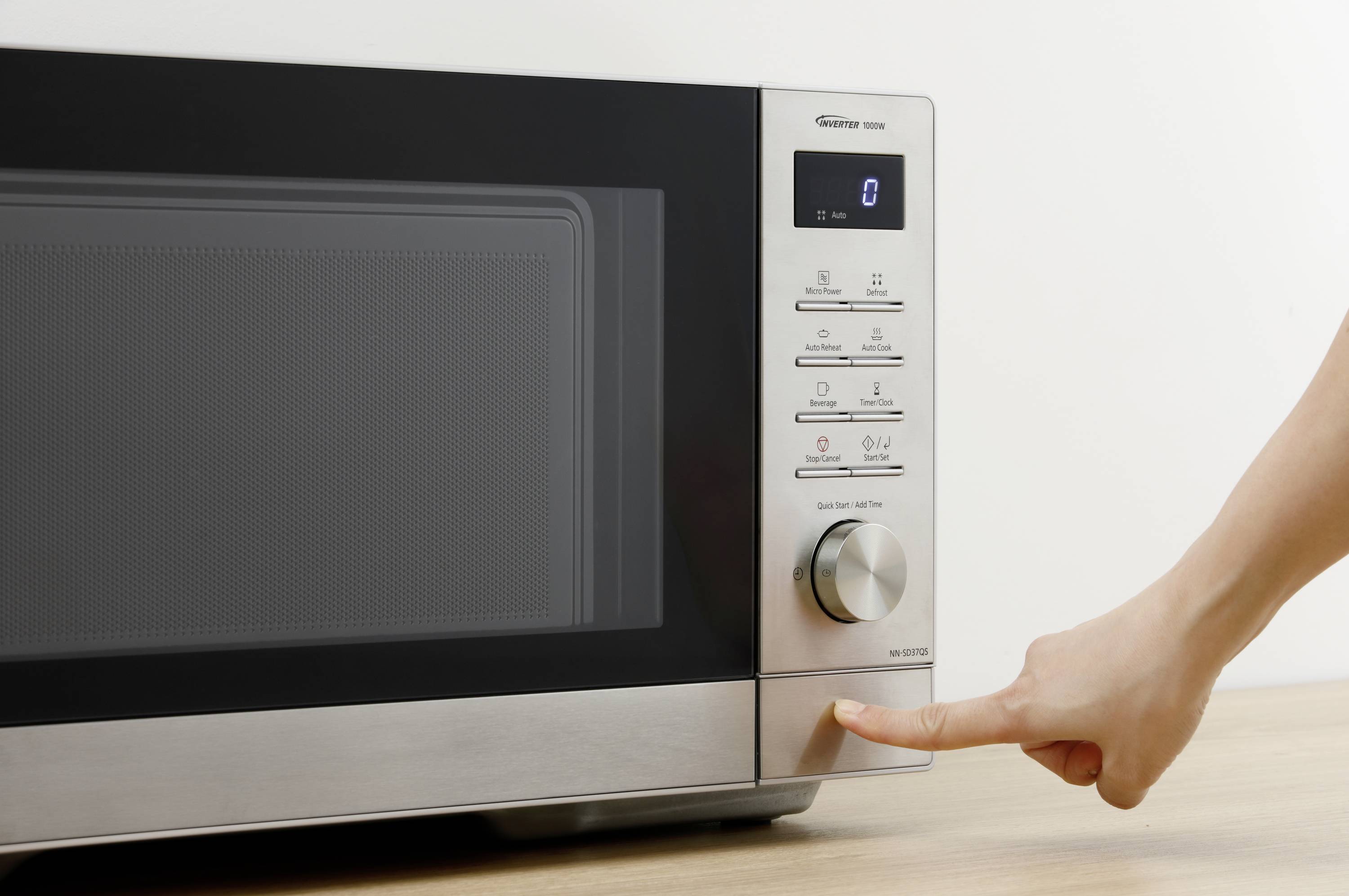 Eine Person drückt den Knopf eines modernen Mikrowellenofens mit digitalem Display und verschiedenen Einstellungsoptionen.