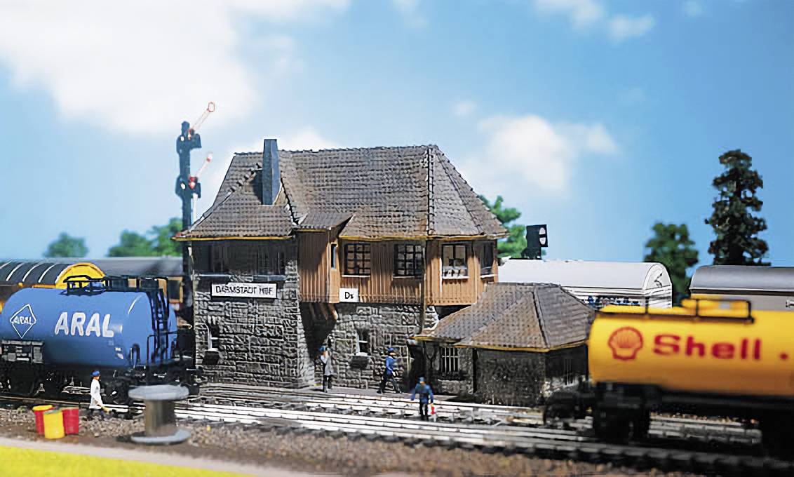 Ein Miniaturbahnhof mit konkretem Gebäude und zwei Modellbahnen. Links ein Zug mit 'ARAL'-Logo, rechts ein Zug mit 'Shell'-Logo.