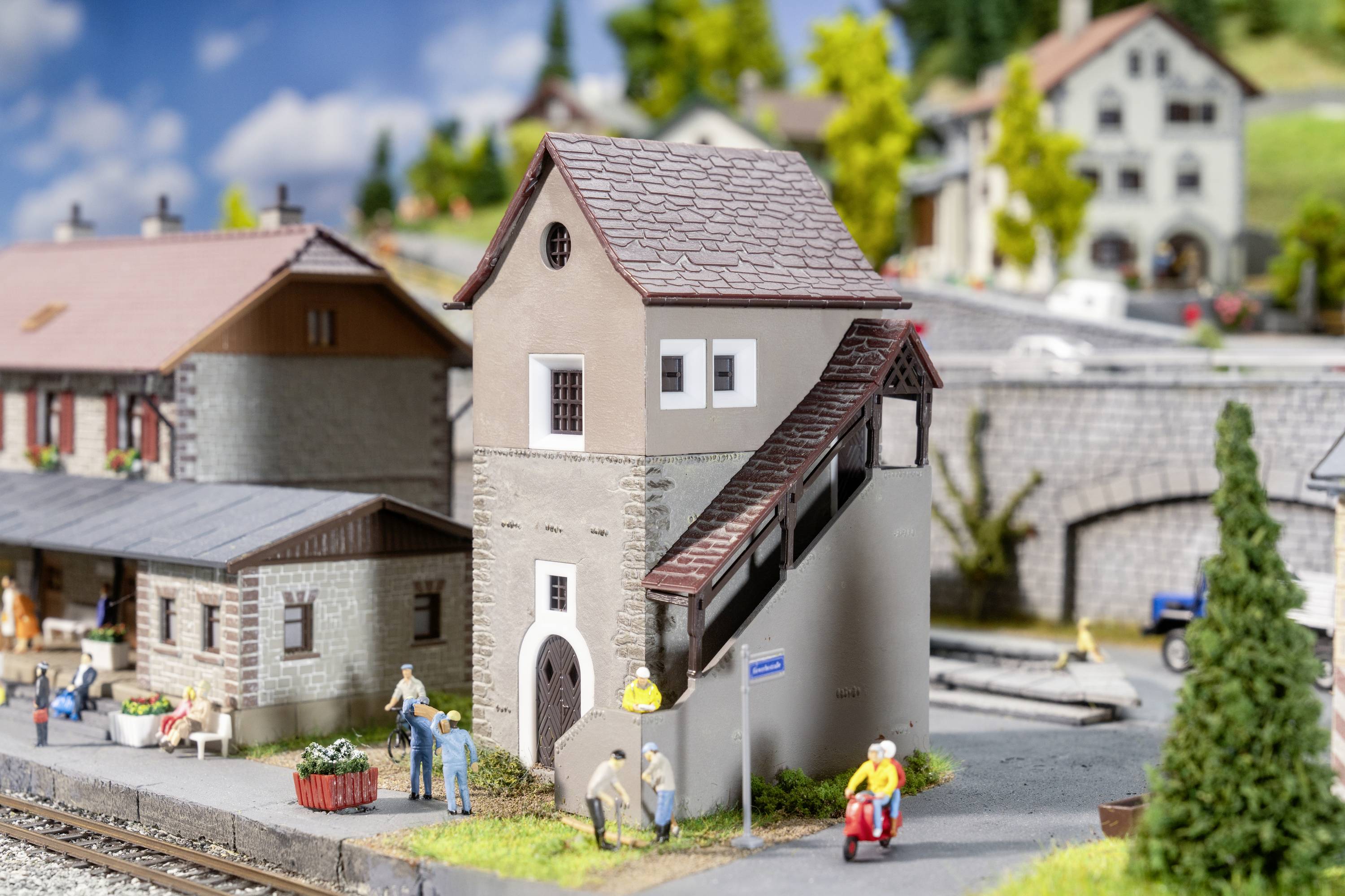Ein Modellbahndiorama zeigt ein Dorf mit Miniaturgebäuden, Personen und Bäumen. Ein Turm mit Treppe steht im Mittelpunkt.