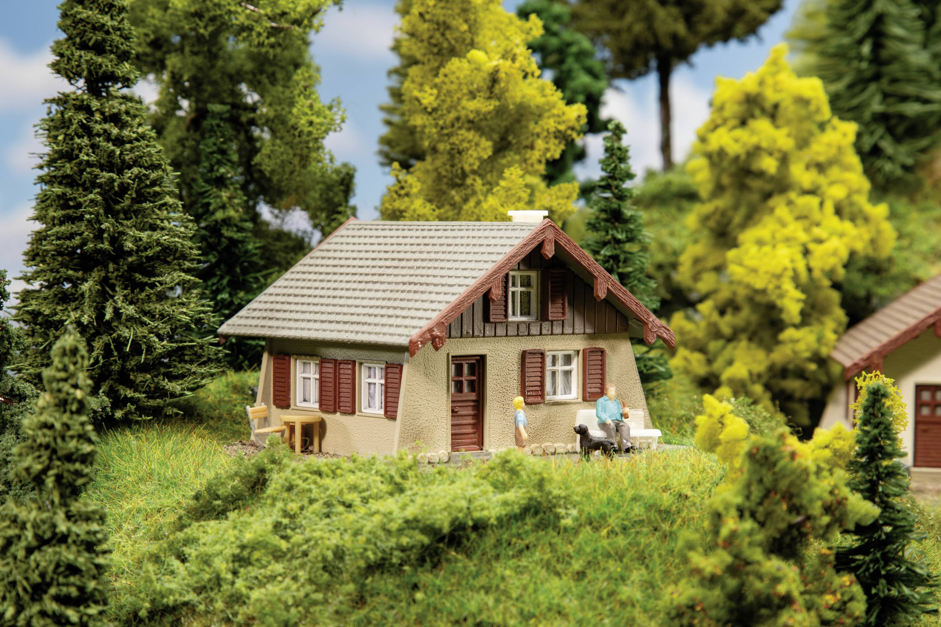 Ein kleines Haus im Wald, umgeben von Bäumen und Wiesen, mit zwei Personen im Garten, die Zeit im Freien genießen.