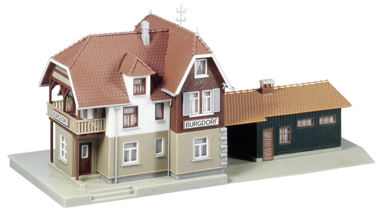 Ein Modell eines kleinen Bahnhofsgebäudes mit rotem Ziegeldach, beigefarbenen Wänden und einem Anbau aus dunklem Holz.