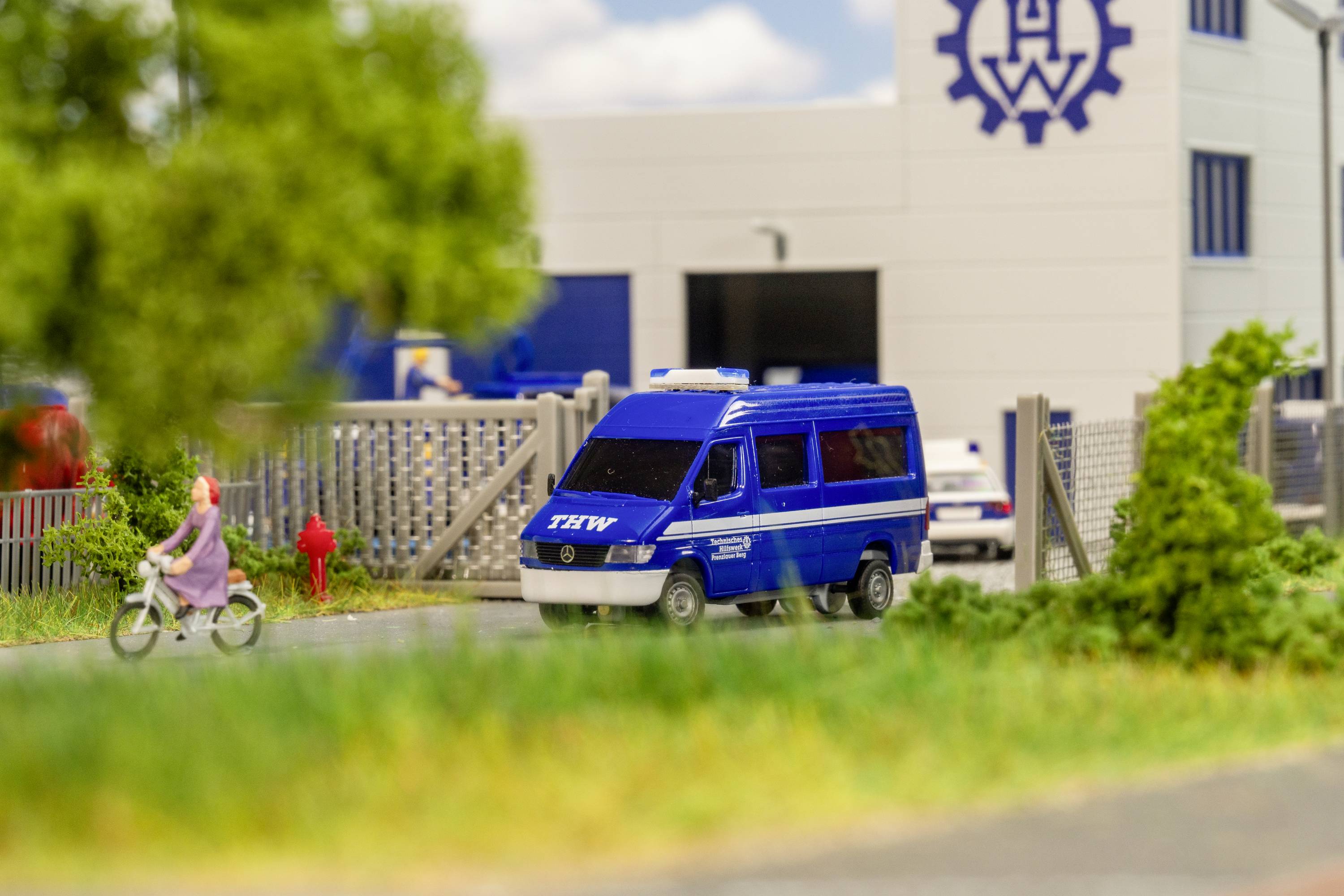 Ein blauer THW-Einsatzwagen parkt vor einem THW-Gebäude. Eine Person fährt auf einem Fahrrad vorbei.