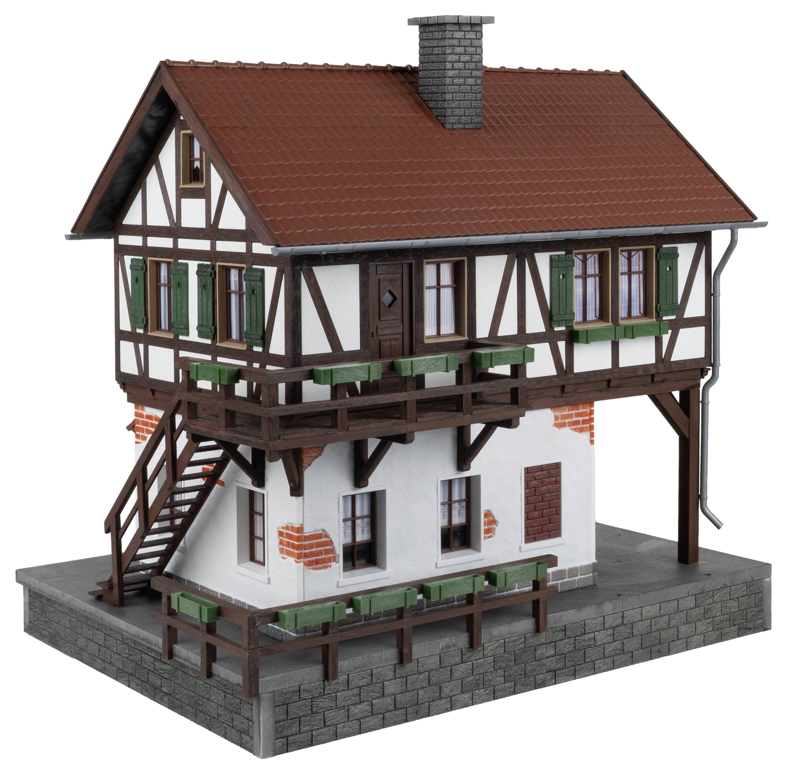 Ein detailliertes Modell eines Fachwerkhauses auf einem Sockel, mit rotem Ziegeldach, grünen Fensterläden und sichtbaren Backsteinstrukturen.