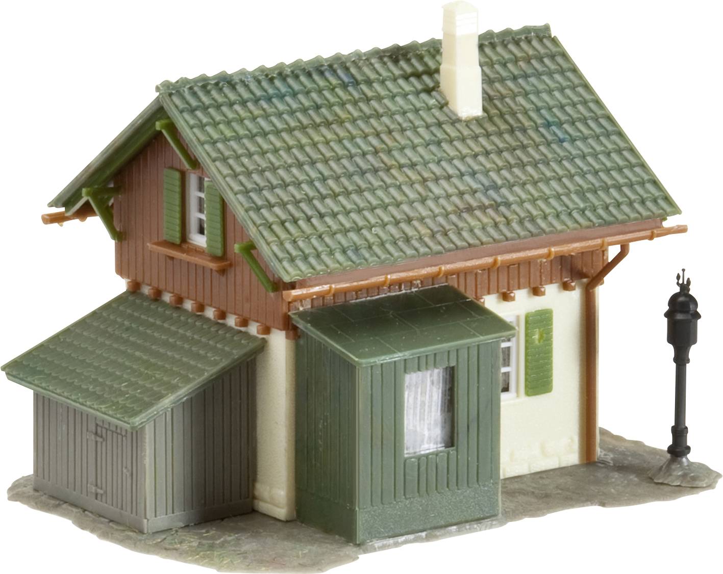 Kleines Modell eines ländlichen Hauses mit grünem Dach, Schornstein und Anbau. Daneben eine schwarze Straßenlaterne.