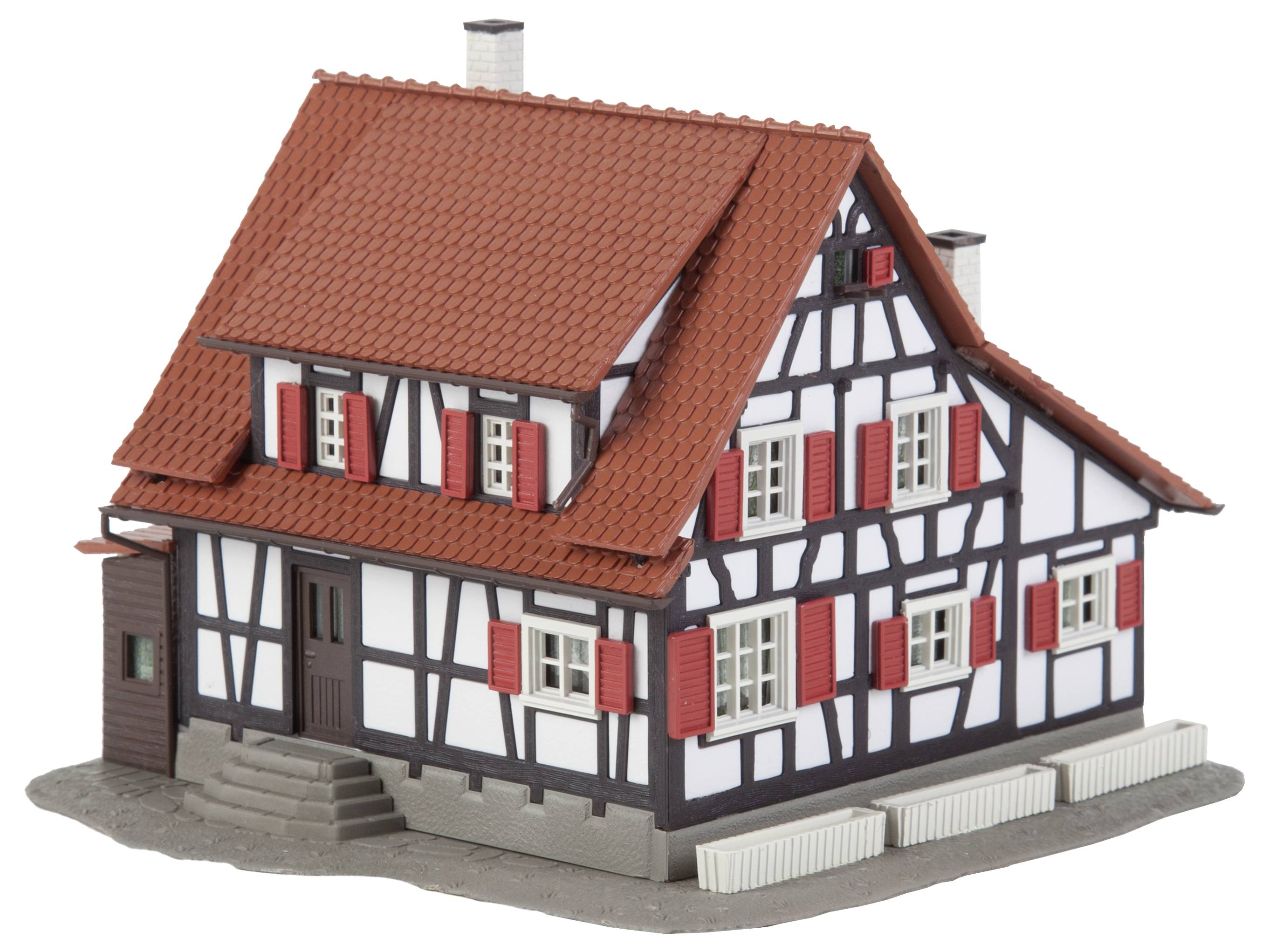 Fachwerkhaus-Modell mit rotem Ziegeldach, weißer Fassade und roten Fensterläden, auf grauer Basis platziert.