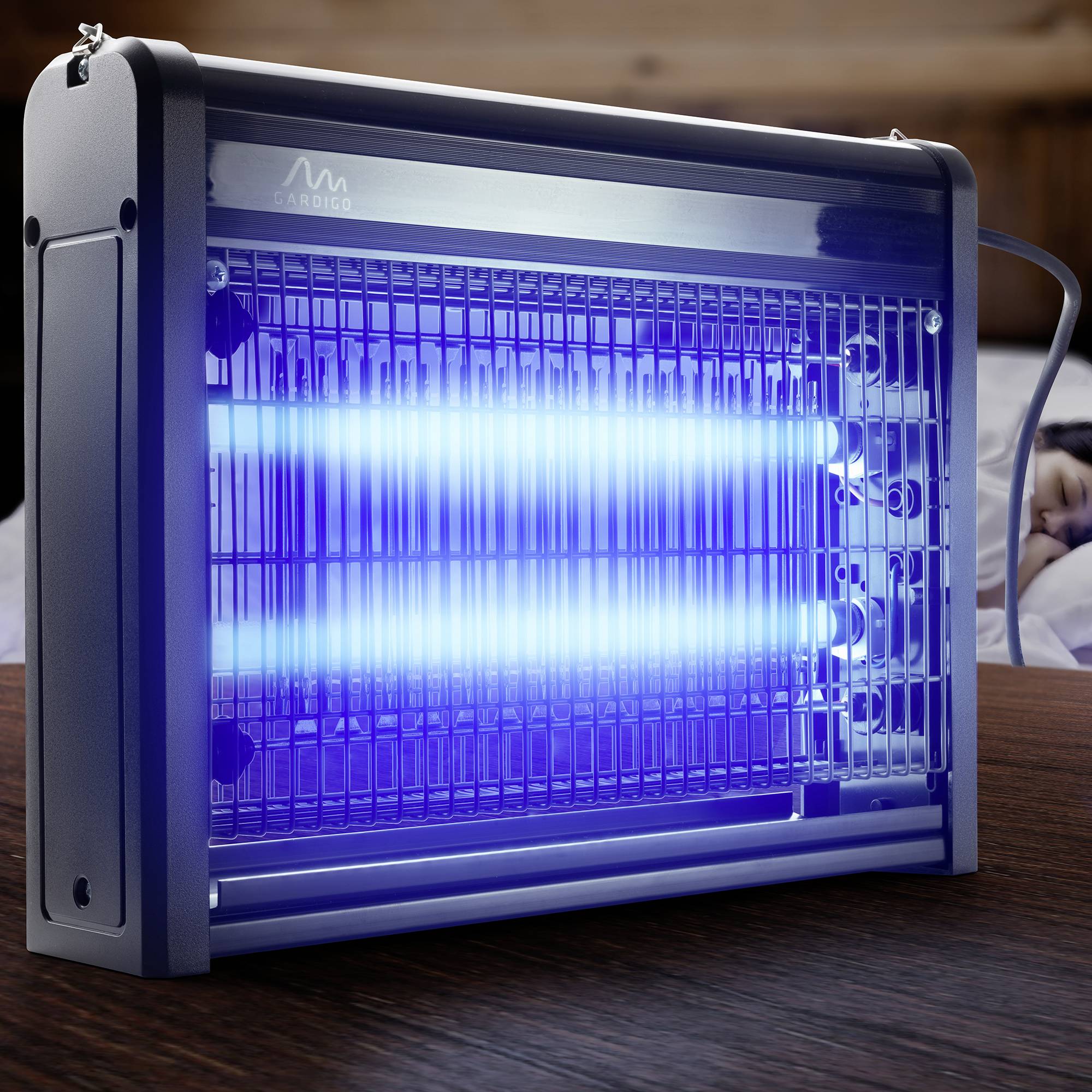 Ein elektrischer Insektenvernichter leuchtet blau auf einem Holztisch, umgeben von Lichtgittern, die Insekten anziehen sollen.