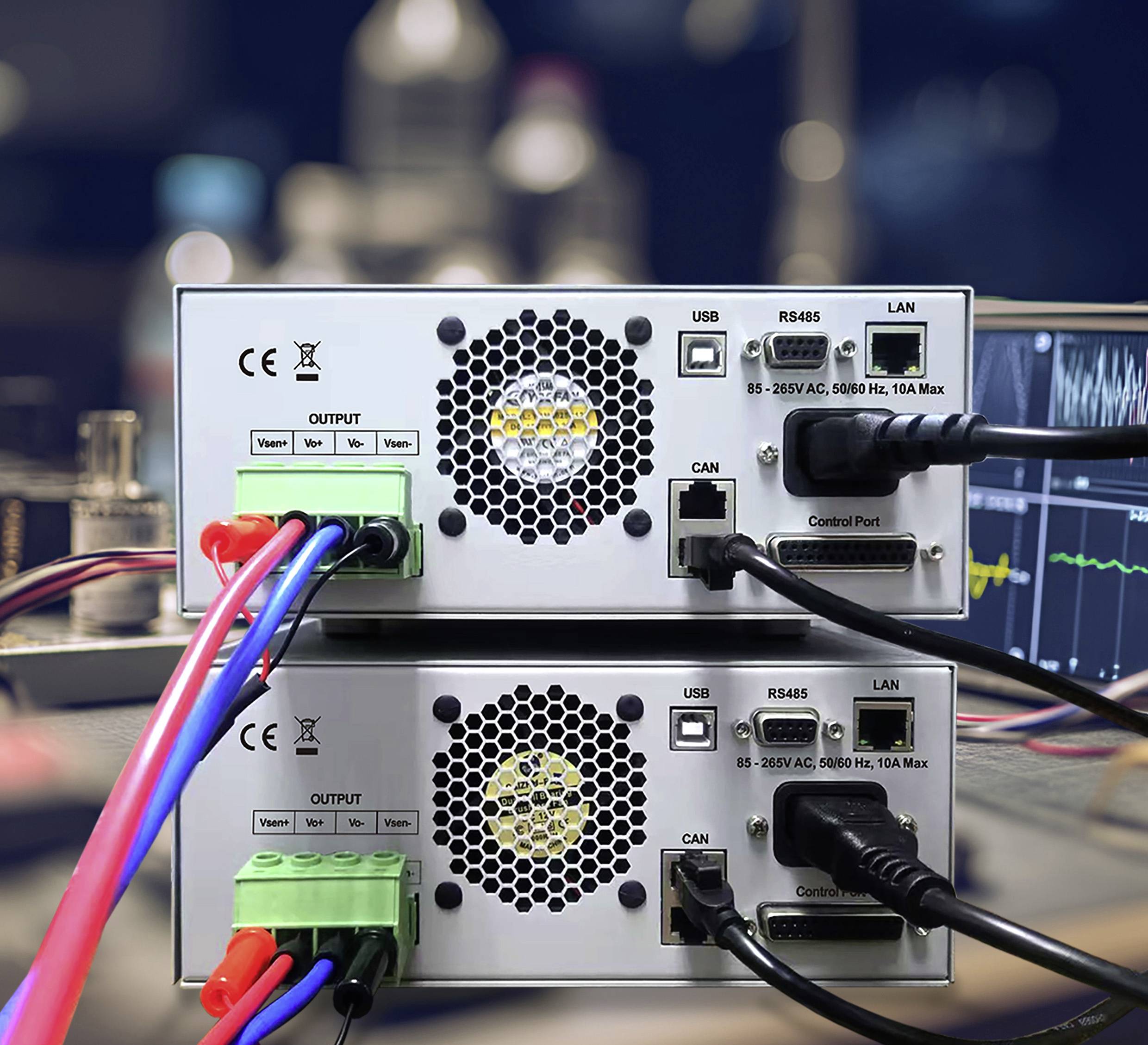 Zwei industrielle Netzteile mit angeschlossenen Kabeln, die USB-, RS485-Anschlüsse und Bedienfelder zeigen; der Hintergrund zeigt ein unscharfes Elektroniklabor.