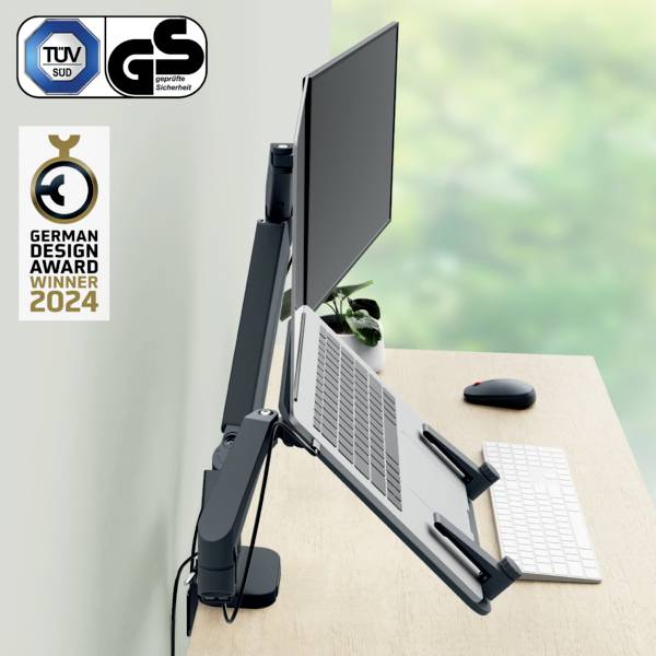 Ein Laptop im vertikalen Ständer, an einen Monitor angeschlossen, auf einem Schreibtisch mit Tastatur. 'German Design Award Winner 2024'.