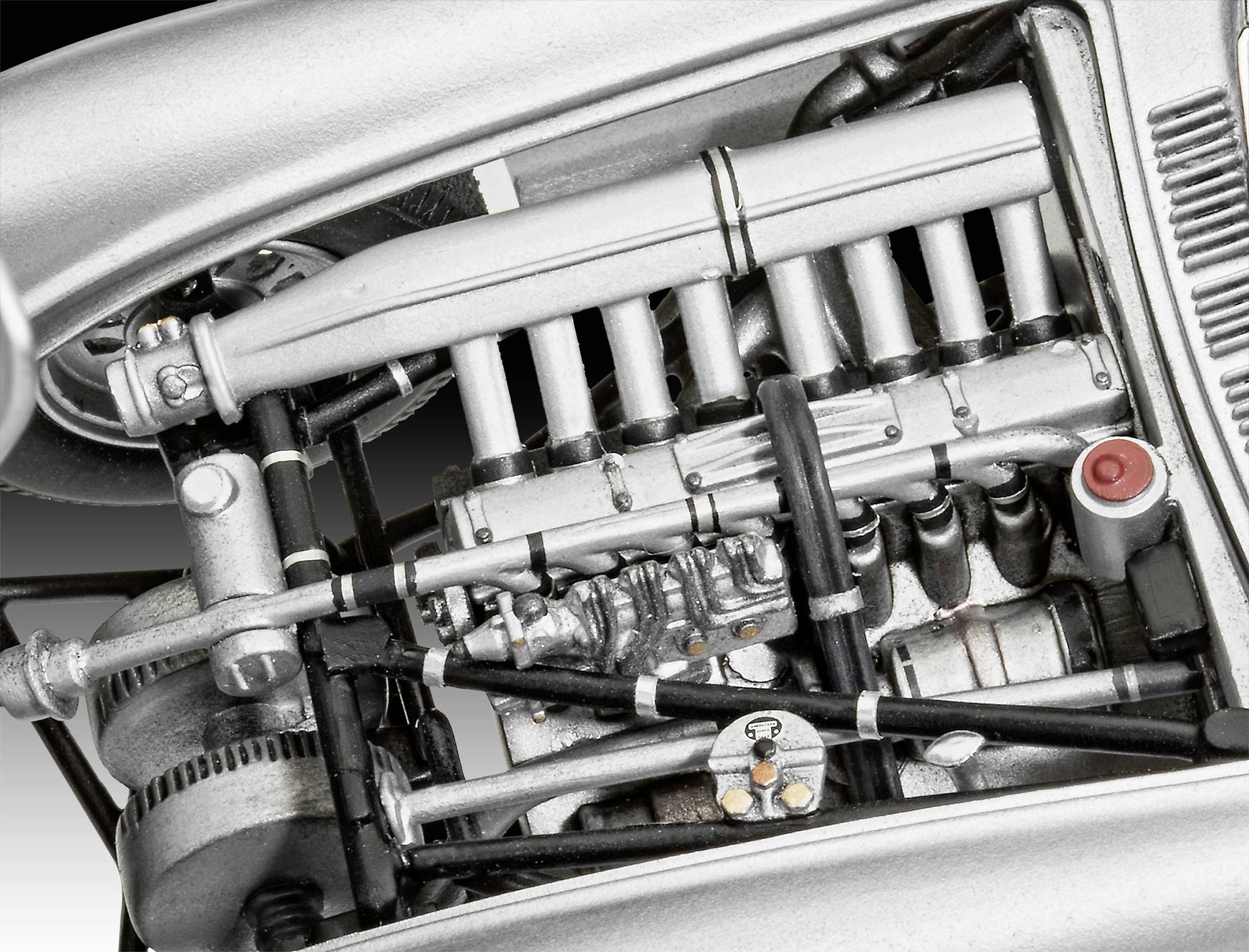 Nahaufnahme eines silbernen Maschinenmotors mit sichtbaren Rohren, Schrauben und einem roten Knopf, zeigt technische Details.