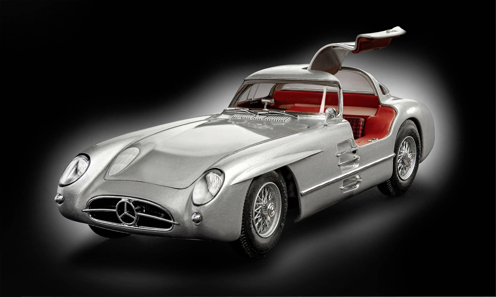 Silberner Sportwagen mit Flügeltüren, rotem Innenraum, auf dunklem Hintergrund. Markantes Design, klassisches Automodell der 1950er Jahre.