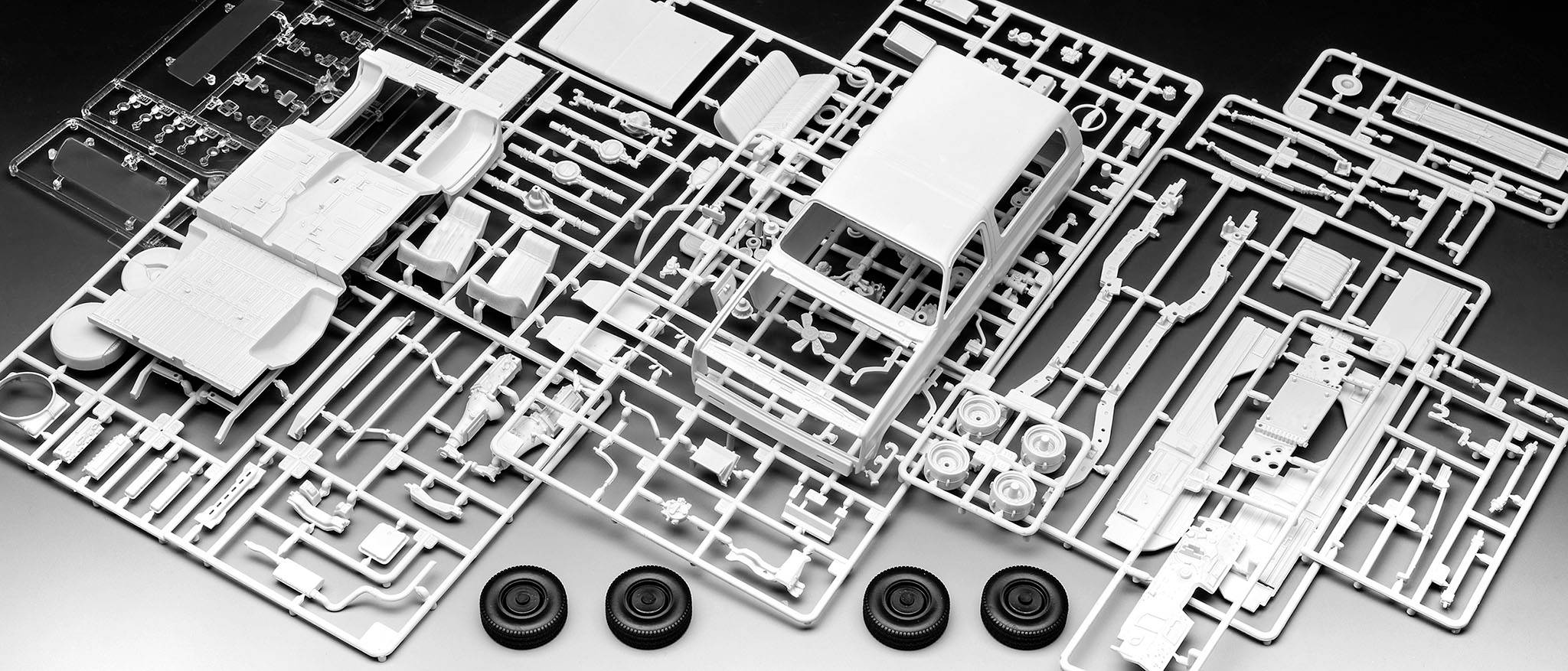 Ein Kunststoff-Modellbausatz mit Teilen für ein Auto, darunter Karosserie, Räder und diverse Kleinteile, bereit zum Zusammenbau.