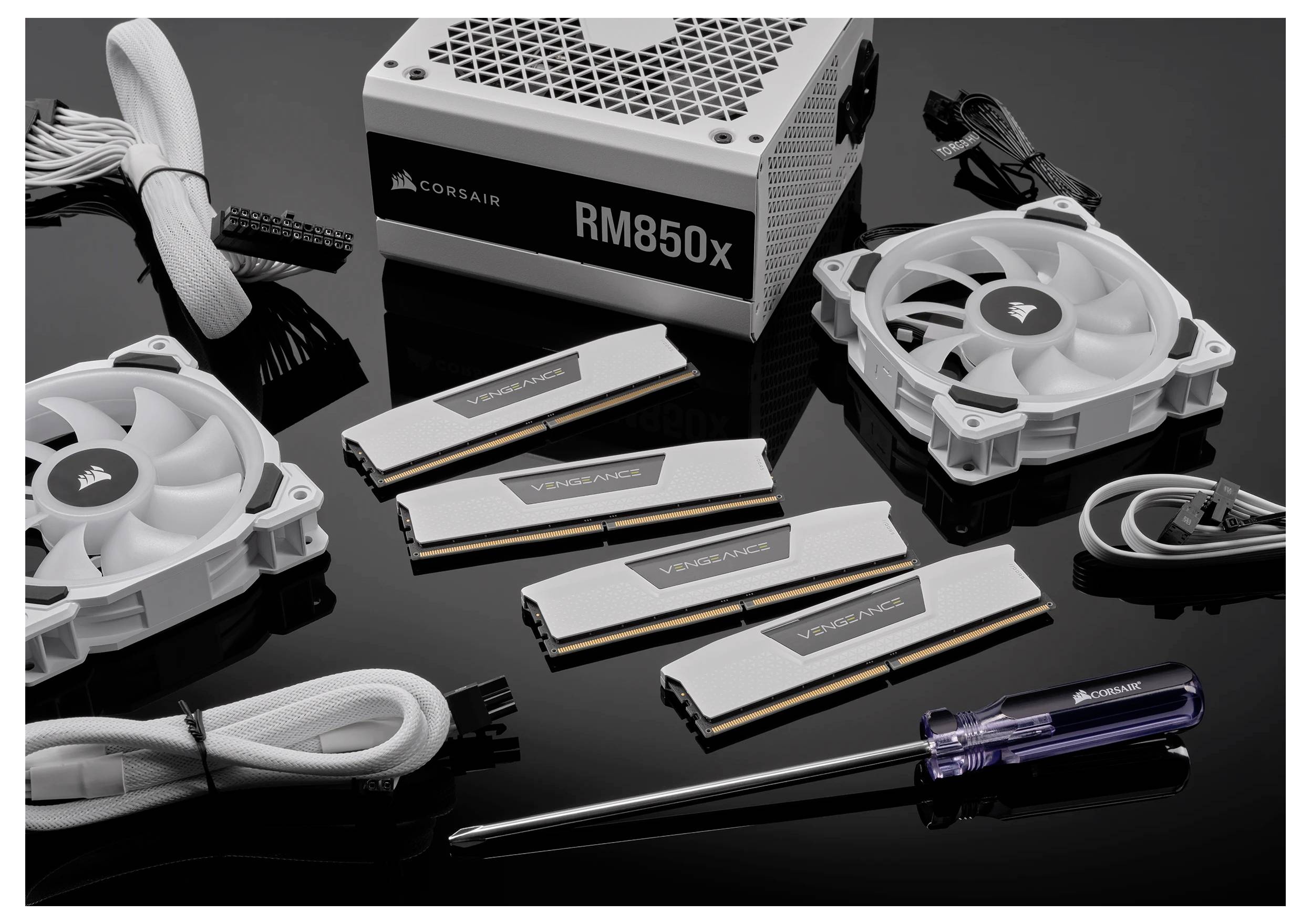 Corsair RM850x Stromversorgung, zwei weiße Kühlventilatoren, vier Vengeance RAM-Module, Kabel und einen Schraubendreher auf einer reflektierenden Oberfläche.