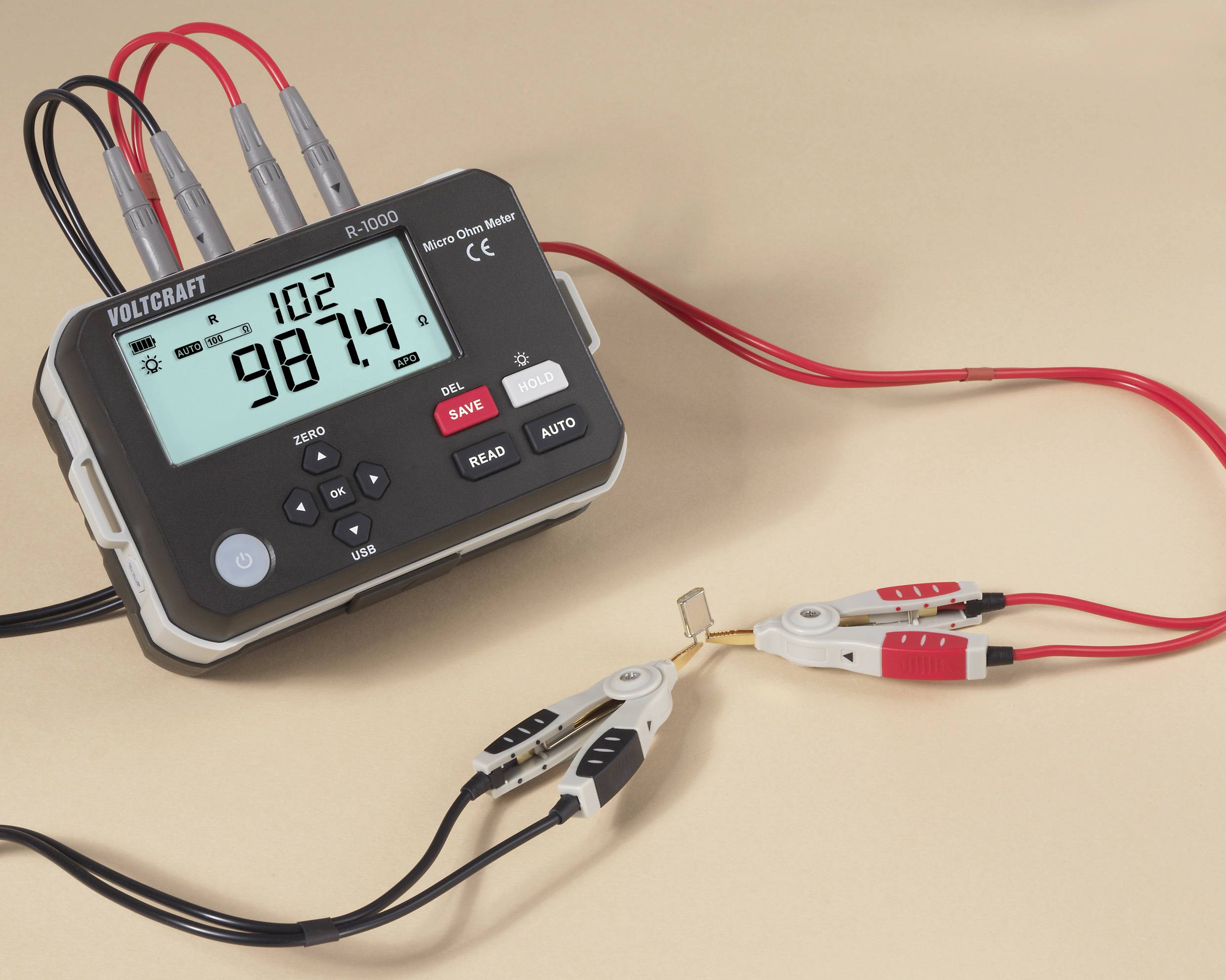 Ein digitales Voltmeter mit roten und schwarzen Messleitungen zeigt '98,74' an. Die Messleitungen sind mit einem kleinen Widerstand verbunden.
