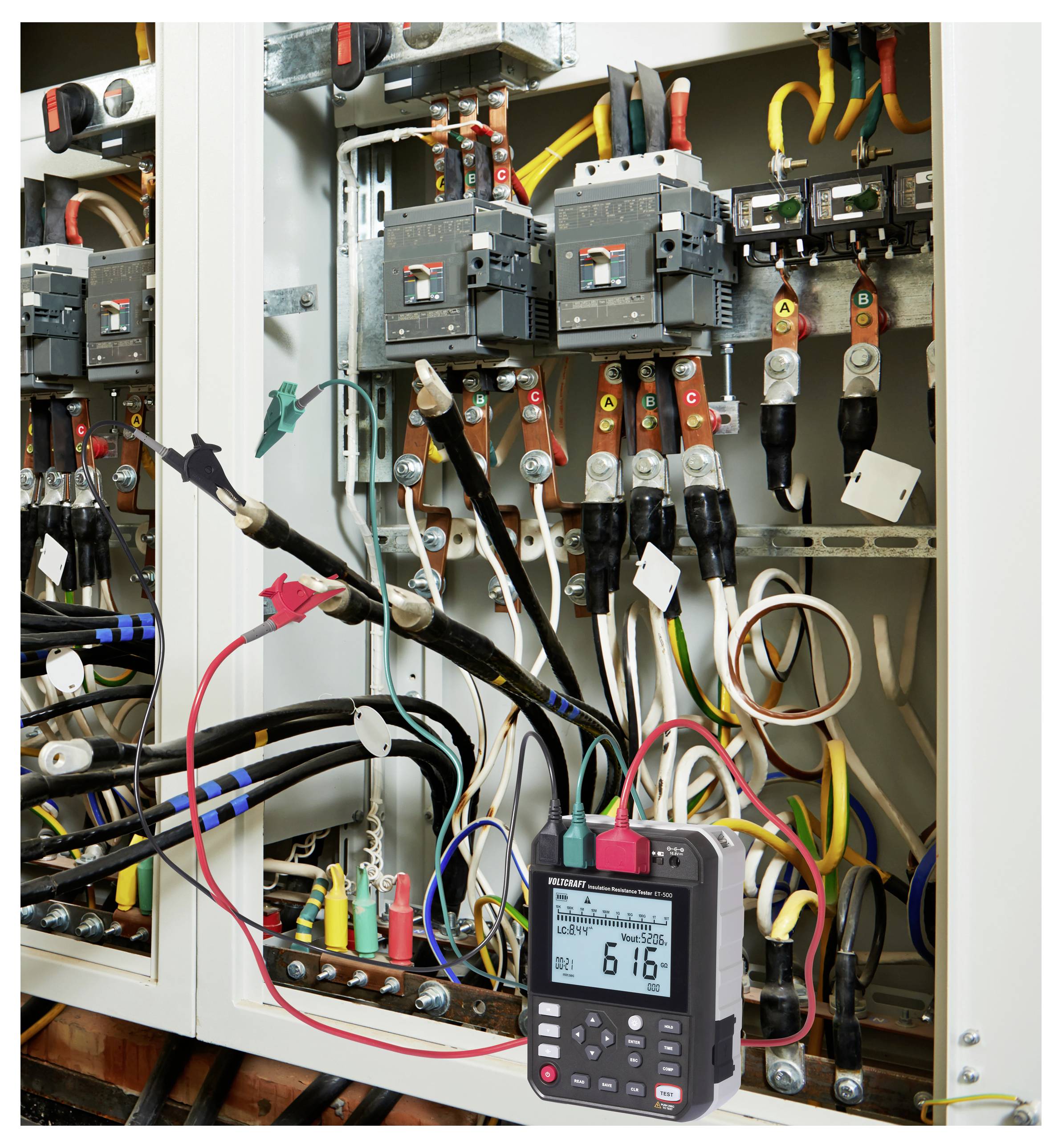 Ein elektrisches Schaltfeld mit mehreren farbigen Kabeln wird mit einem digitalen Multimeter getestet, das einen Messwert von „6,16