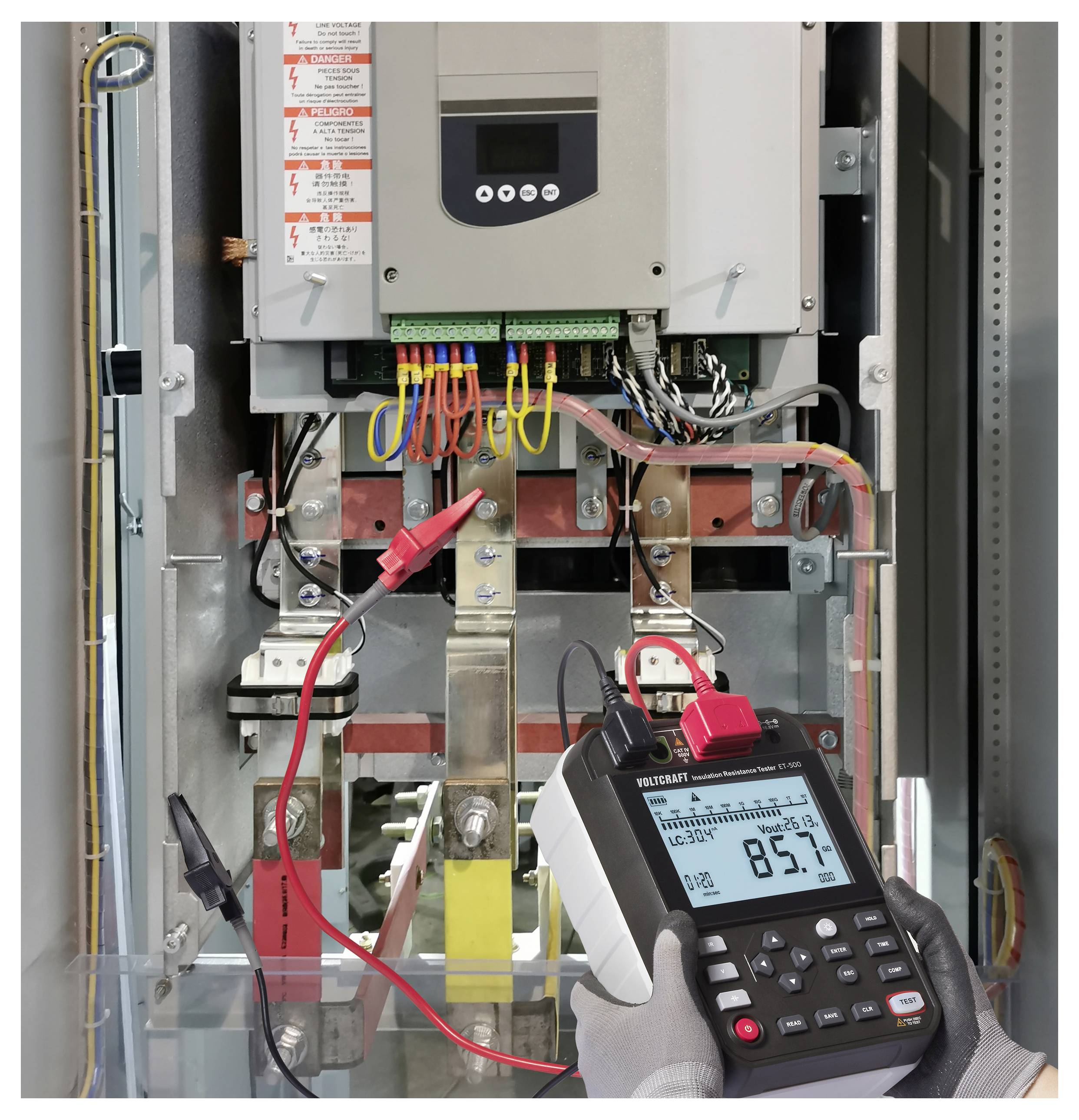 Eine Person nutzt ein digitales Multimeter zur Spannungsmessung in einem Schaltschrank und zeigt eine Anzeige von 85,7 Volt. Sicherheitskennzeichnungen sind sichtbar.