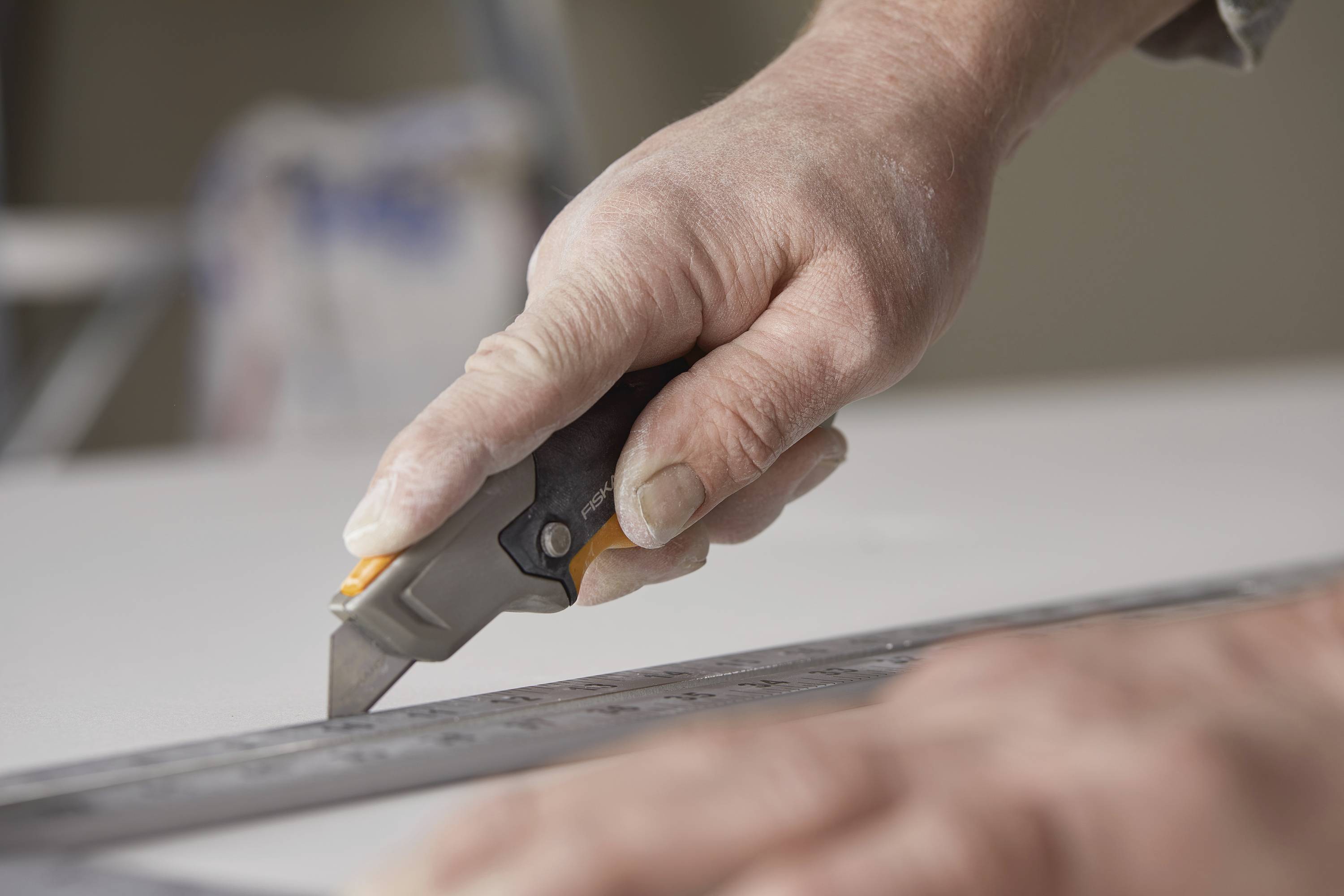 Hand mit Cutter-Messer schneidet entlang Lineal auf weißem Untergrund.