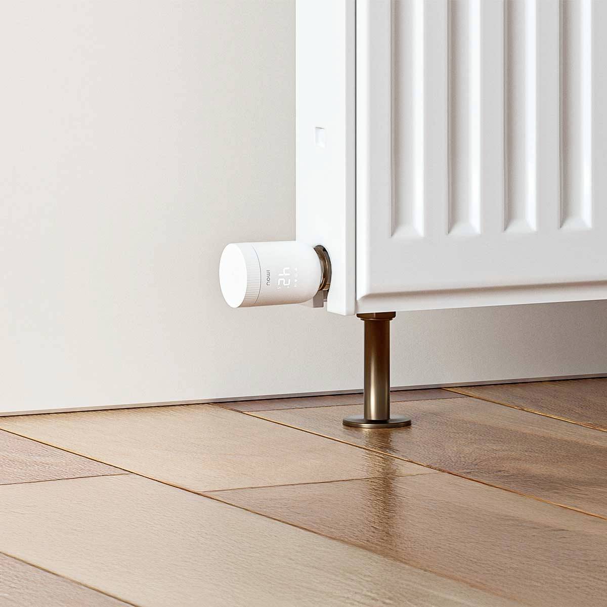 Ein weißer Heizkörper in einem Raum mit Holzfußboden. Ein digitales Thermostat zeigt die Temperatur an.