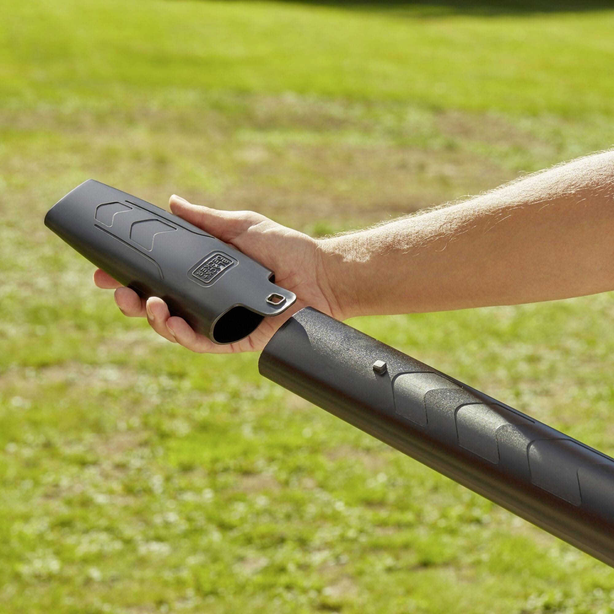 Person montiert Abdeckung auf ein Ofenrohr in einem Garten. Hauptfokus liegt auf der Hand und dem Rohr, umgeben von grünem Gras.