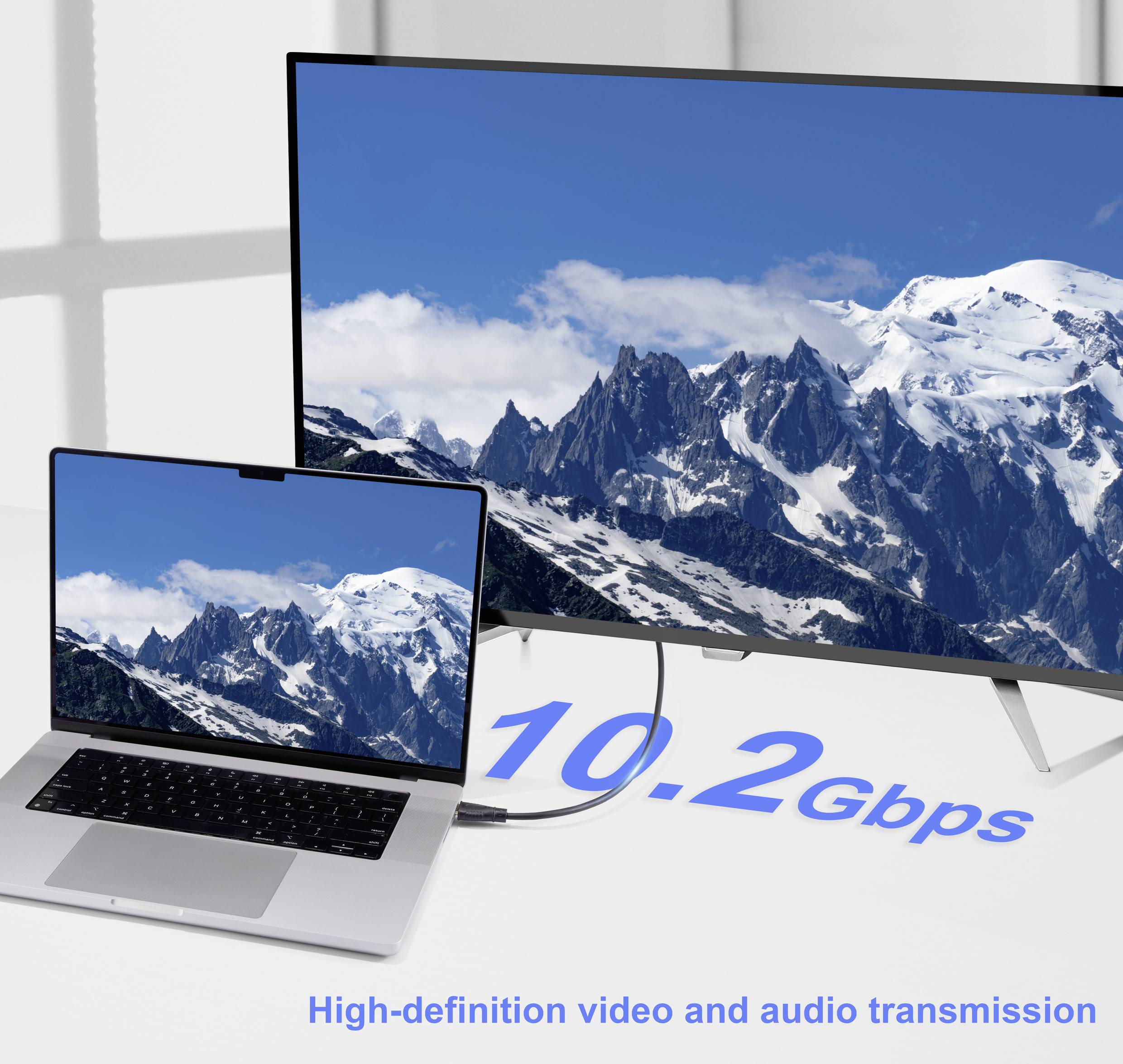 Ein Laptop ist mit einem größeren Monitor verbunden, beide zeigen eine verschneite Berglandschaft. Der Text liest '10,2 Gbit/s' und deutet auf eine hochgeschwindigke Datenübertragung hin.