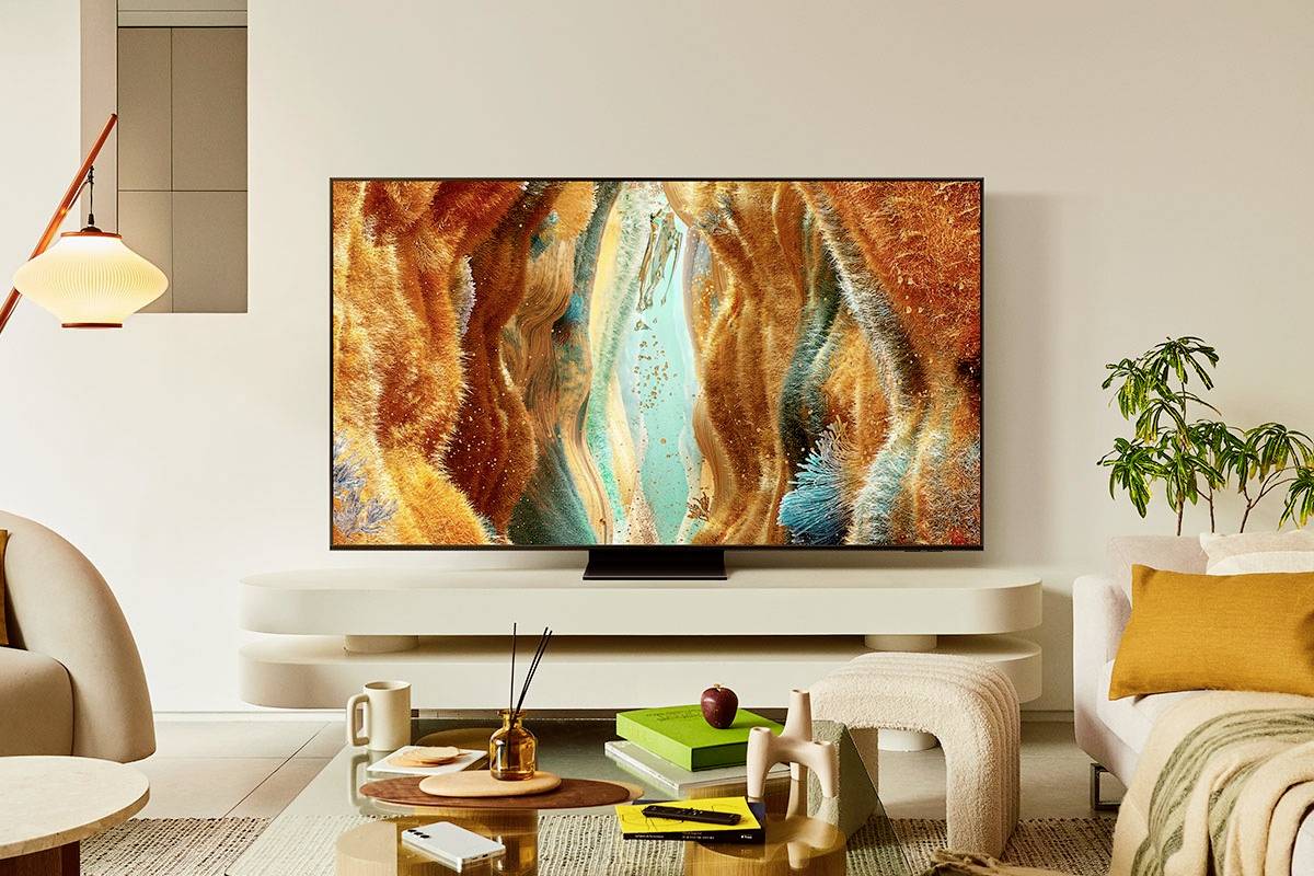 Wohnzimmer mit modernem Fernseher auf weißem Regal, zeigt abstrakte Kunst in warmen Farben. Geflechtsessel und Pflanze neben Sofa.