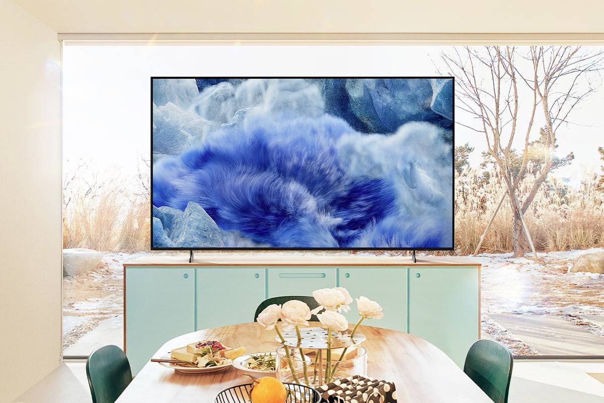 Ein Fernseher zeigt ein Bild mit blauem Wasser. Der Fernseher steht auf einem Sideboard in einem hellen Raum mit Blick ins Freie.