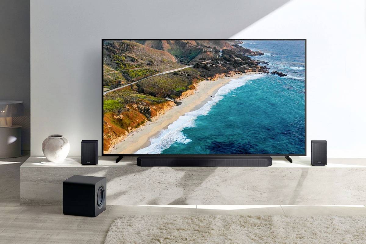 Ein moderner Flachbildfernseher zeigt eine Küstenszene mit klarem blauen Wasser und Klippen. Umgeben von Lautsprechern in einem Wohnzimmer.