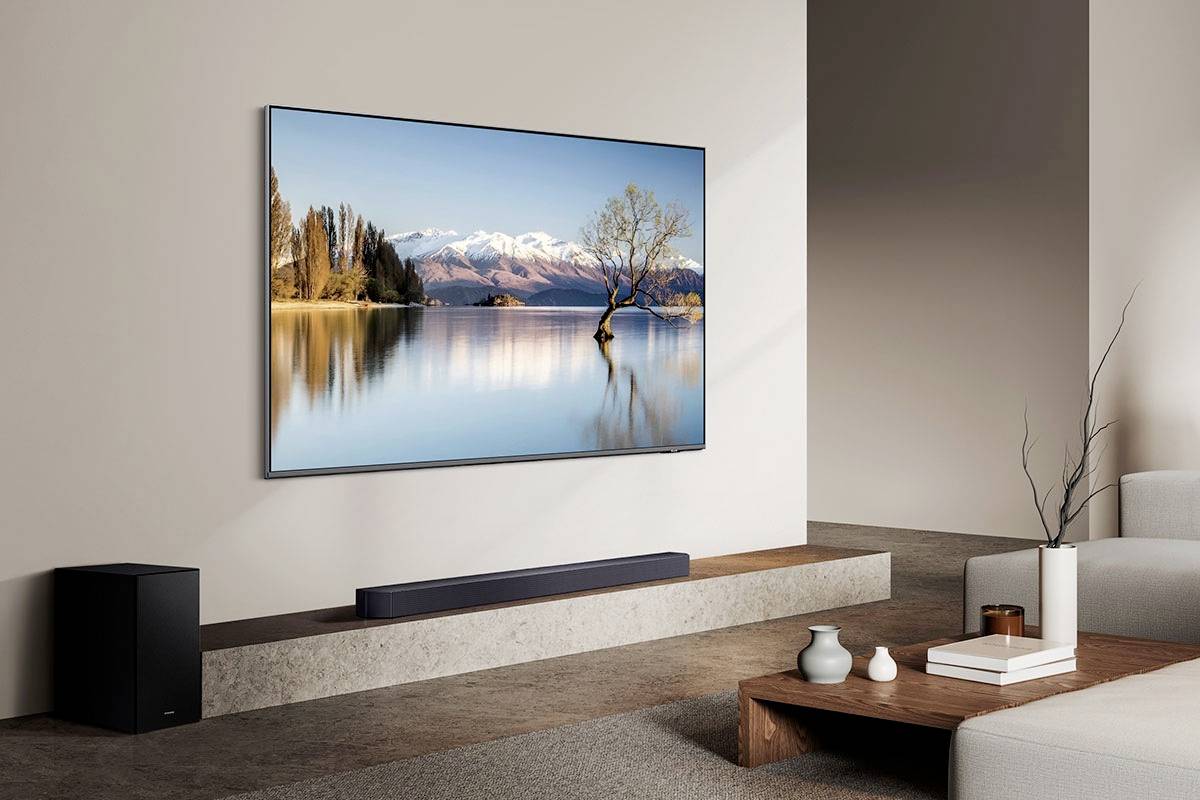 Ein modernes Wohnzimmer mit einem großen Flachbildfernseher an der Wand. Darauf ist eine Landschaft mit einem See und schneebedeckten Bergen zu sehen.