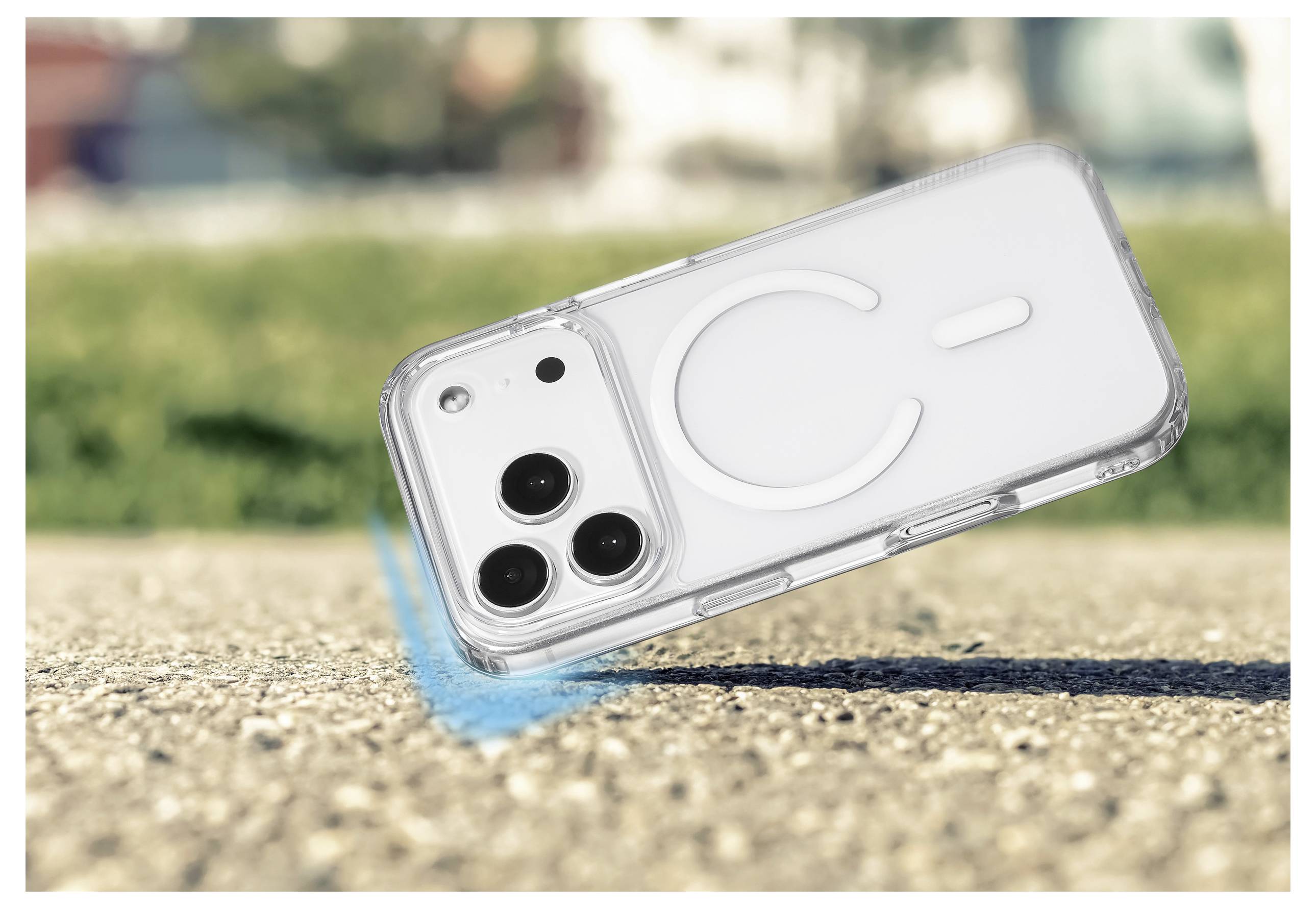 Ein weißes Smartphone mit drei Rückkameras wird in einer transparenten Hülle gezeigt, schräg auf einer Betonoberfläche liegend, mit einem verschwommenen grünen und urbanen Hintergrund.