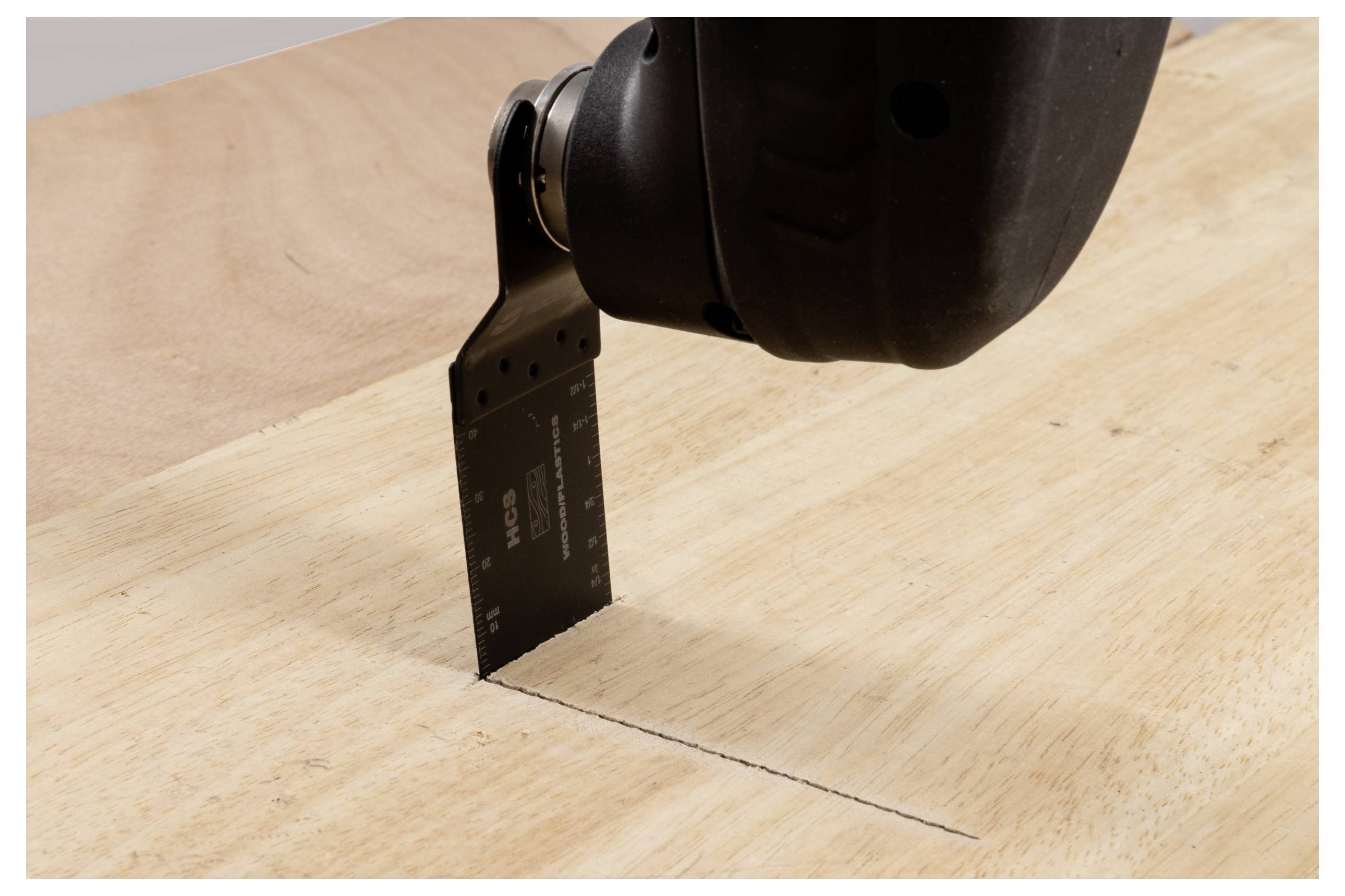 Ein Elektrowerkzeug mit einer flachen Klinge schneidet in eine Holzplanke und zieht eine gerade Linie. Das Werkzeug ist nach unten geneigt und zeigt präzises Schneiden.