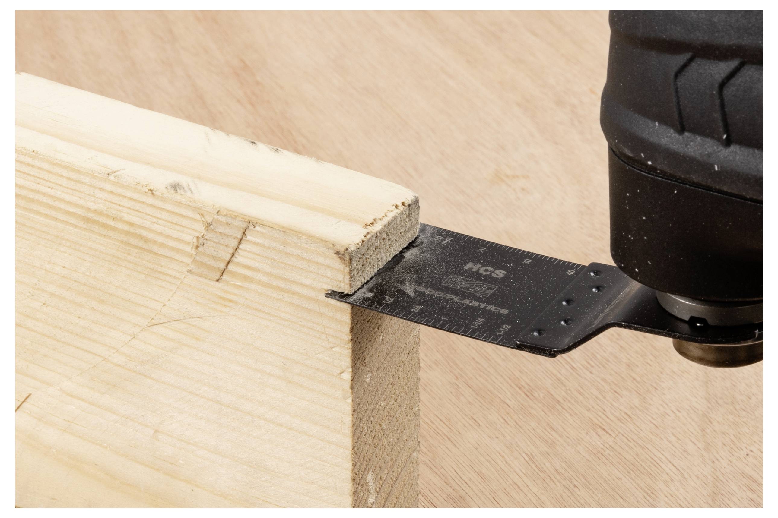 Eine Elektrowerkzeug mit einer schwarzen Klinge schneidet durch ein hellfarbiges Holzstück auf einer flachen Oberfläche.