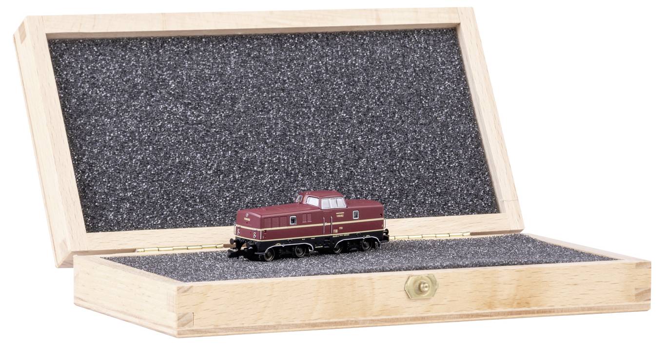Kleine Modelllokomotive in einer offenen Holzbox mit schwarzem Schaumstoff ausgekleidet. Die Lokomotive ist dunkelrot und detailliert gestaltet.