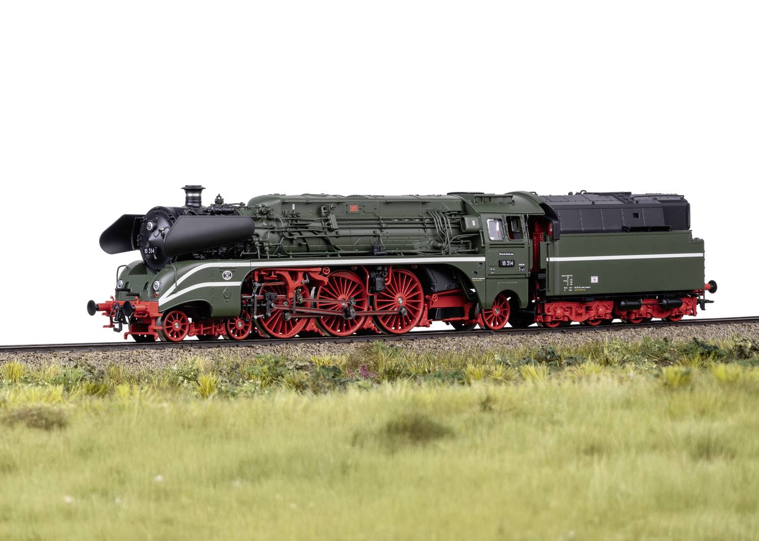 Ein grünes Modell einer Dampflokomotive mit roten Rädern auf einem Gleis, umgeben von Gras.