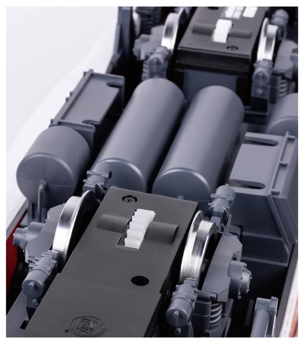 Nahaufnahme von Teilen einer grauen, industriell gefertigten Maschine mit Metallrollen und mehreren Zylindern. Funktion unbekannt.