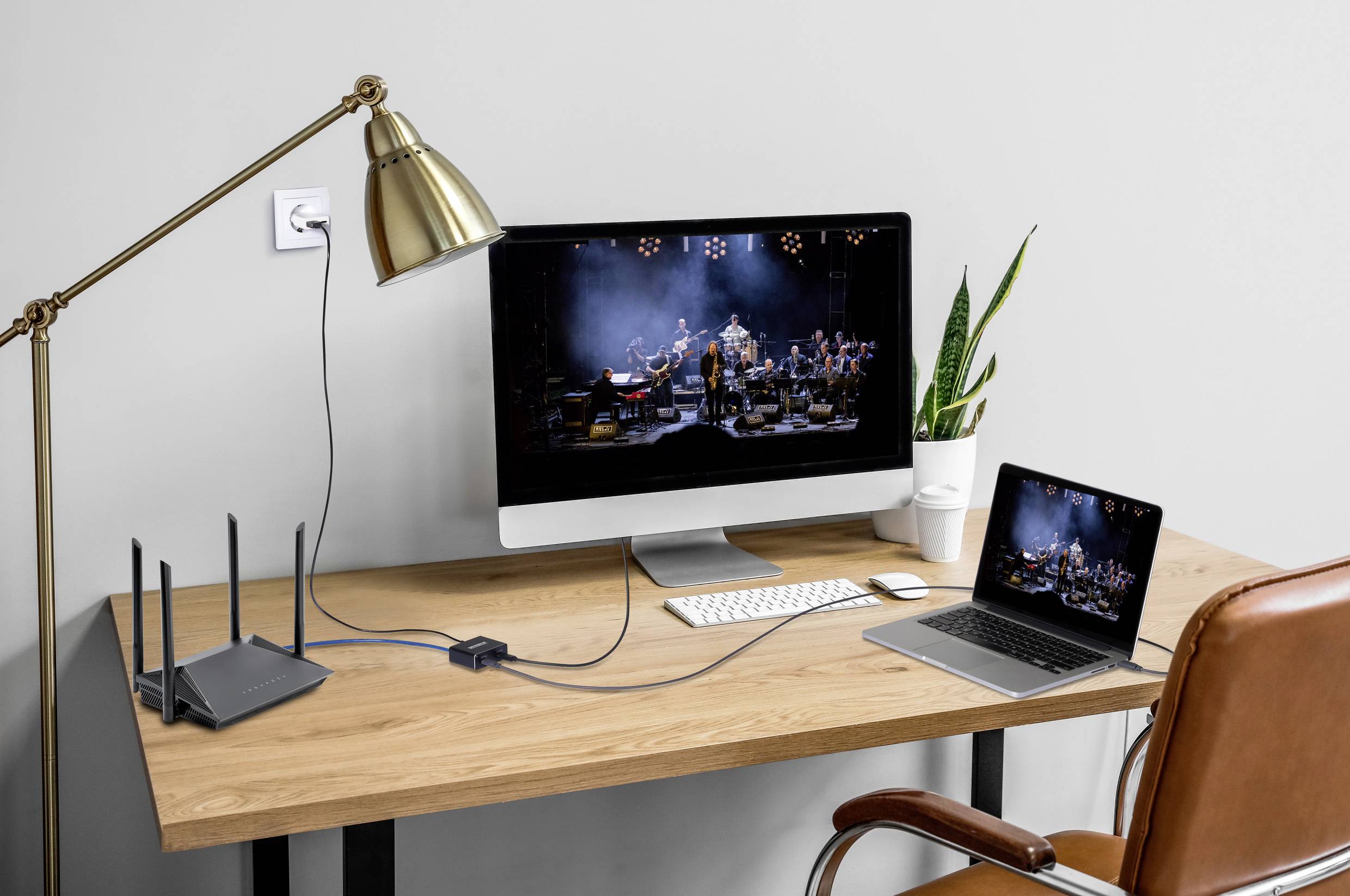 Ein Home-Office-Setup mit einem Desktop-Monitor und einem Laptop, die ein Orchester anzeigen, sowie einer Tastatur, Maus, Lampe und einer Pflanze auf einem Holzschreibtisch.